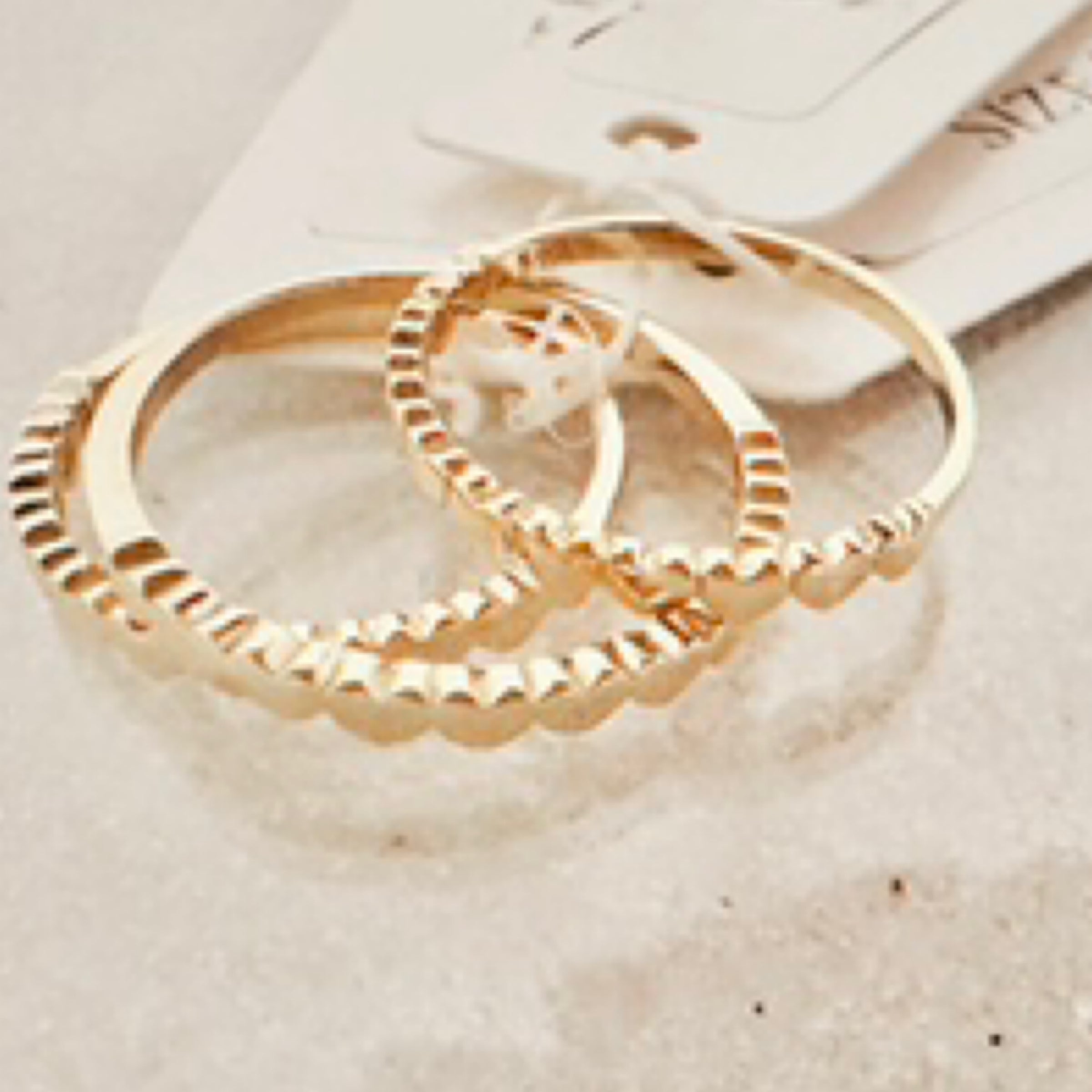 Gold ring with heart scalloping along top. Pictured against white sand.
