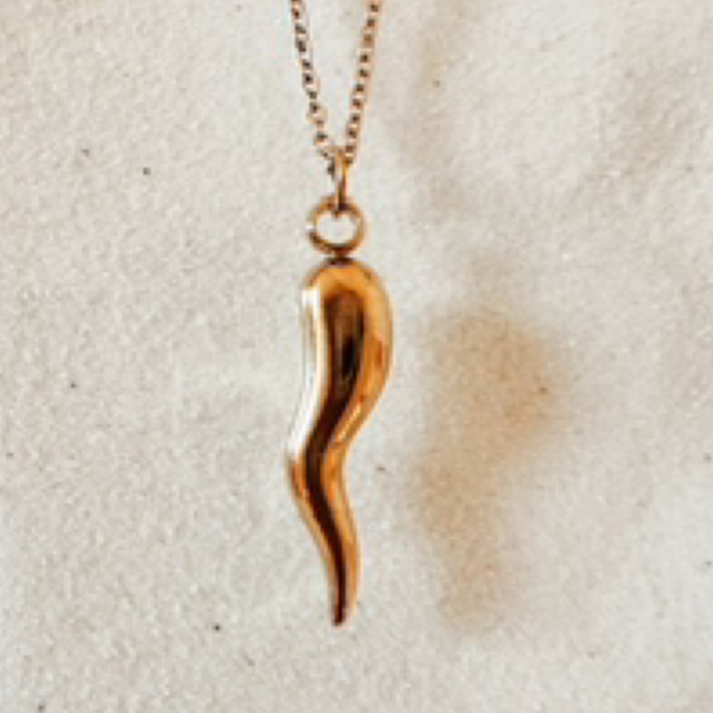 Delicate gold chain with a gold pepper charm. Pictured against white sand.