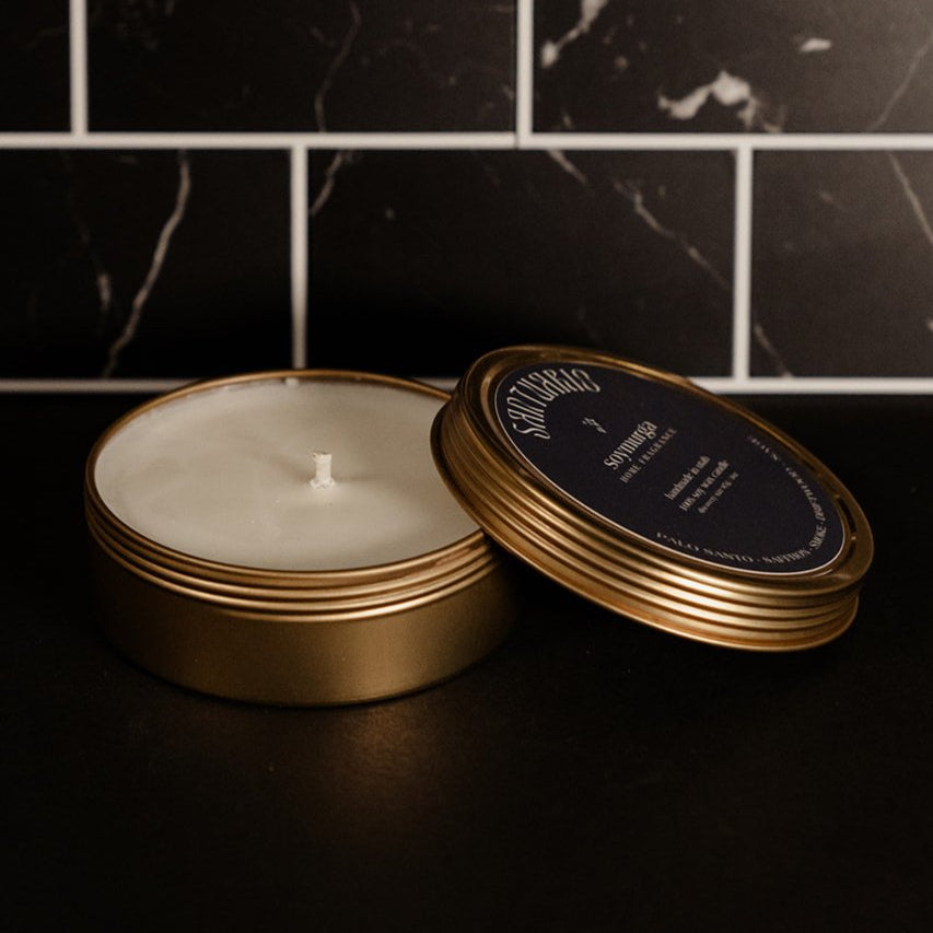 Small gold tin candle with a navy blue label. Pictured against a black marble back splash.