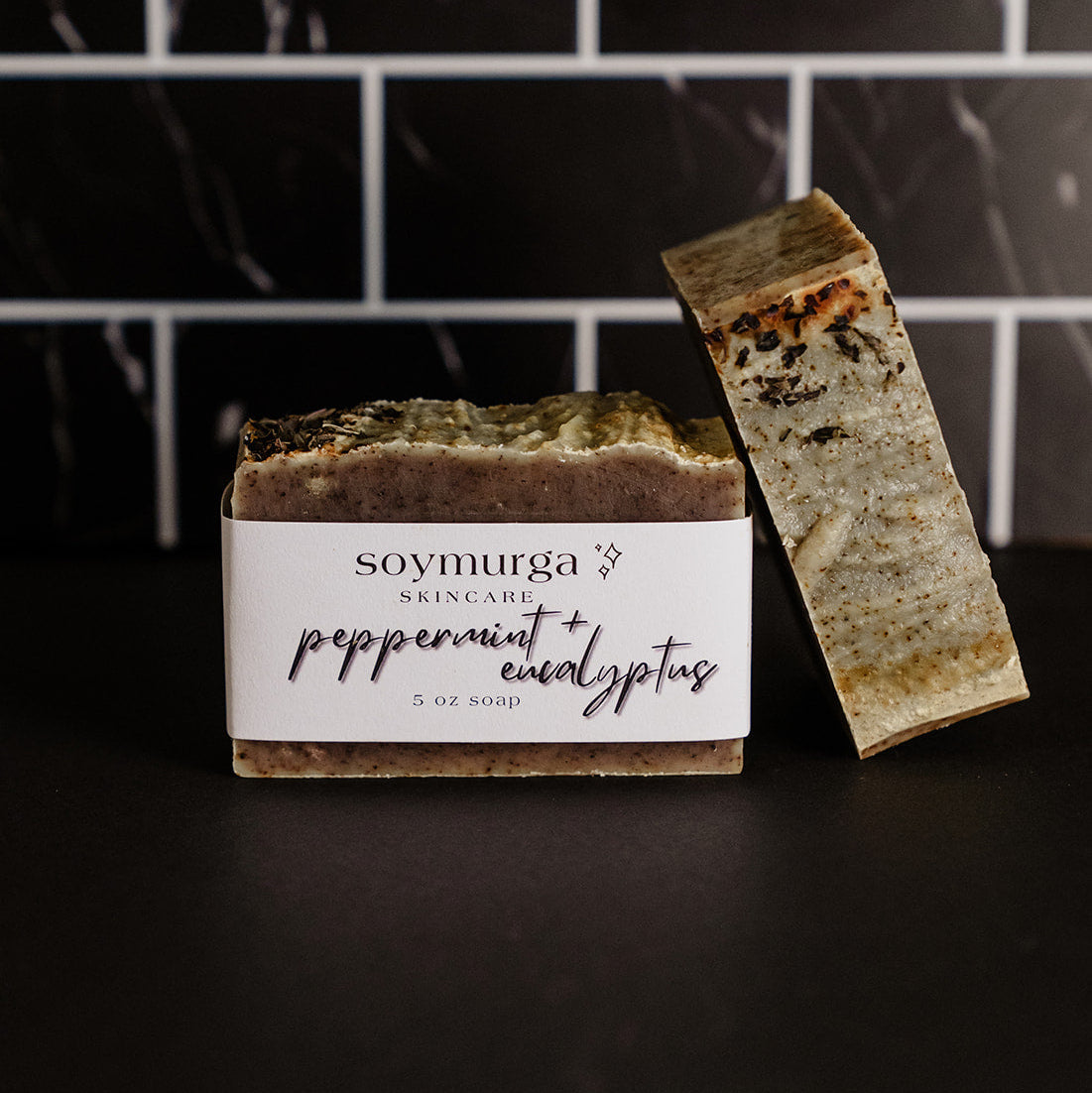 Peppermint + Eucalyptus soap bar on a black countertop with black marble subway tile in the background.