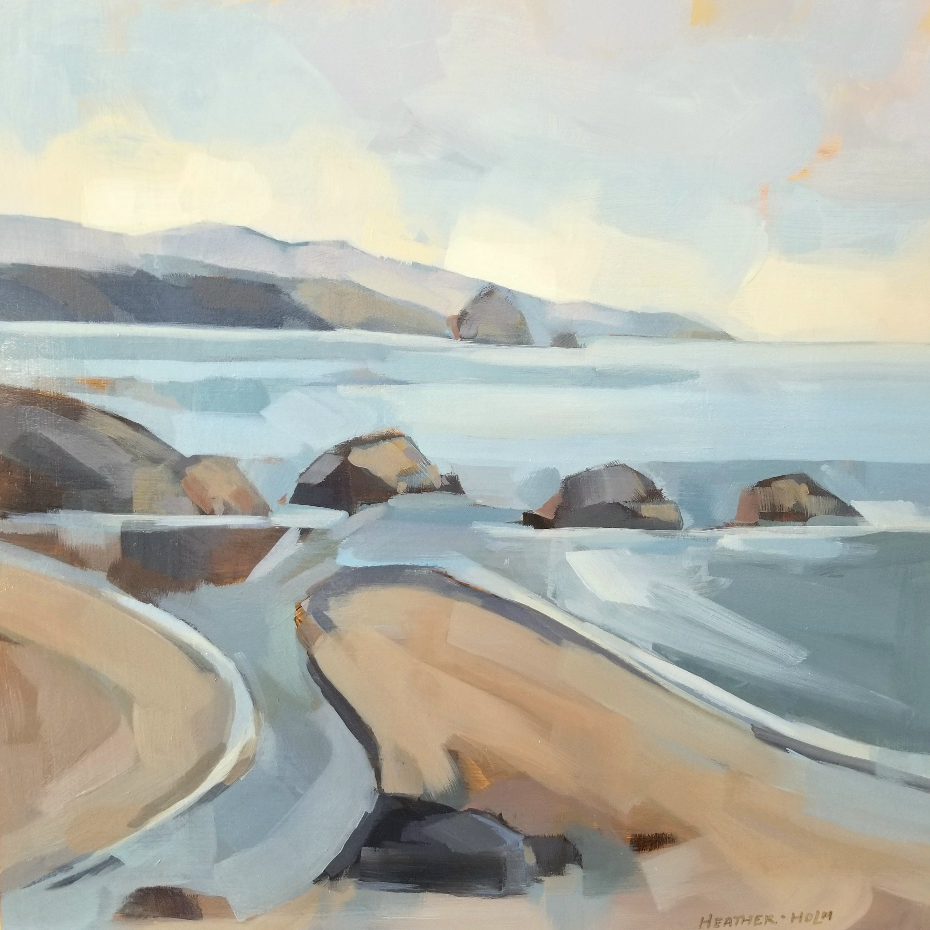 An ocean view from a sandy beach with big boulders. The water is deep blue and the sky is golden.