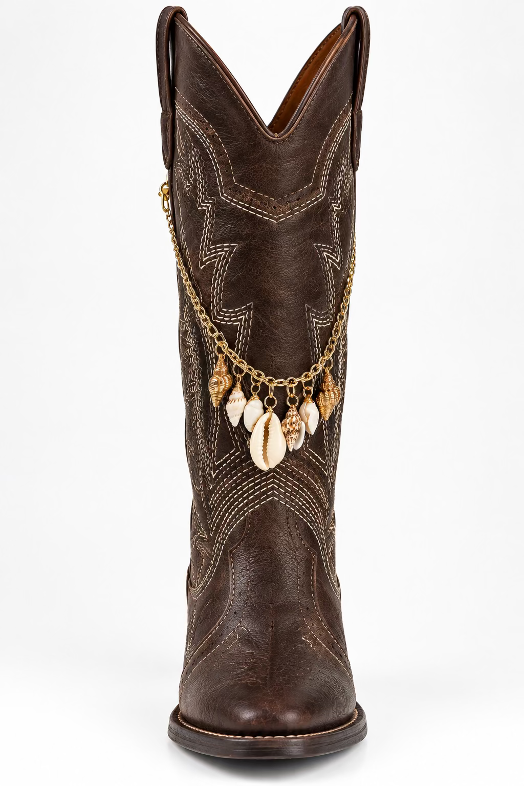 A dark brown leather cowboy boot with intricate white decorative stitching, a pointed shaft, rounded toe, and dark sole, adorned with a gold chain featuring dangling cream and tan seashell charms. The boot is photographed upright against a plain white background.