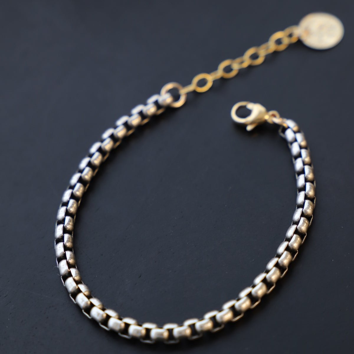 Introducing the Nova Chain Bracelet - a stunning, two tone accessory featuring a round silver box chain with a gold lobster clasp and end chain with a coin drop. The perfect blend of elegance and edge, this bracelet will elevate any outfit with its sleek, modern design.