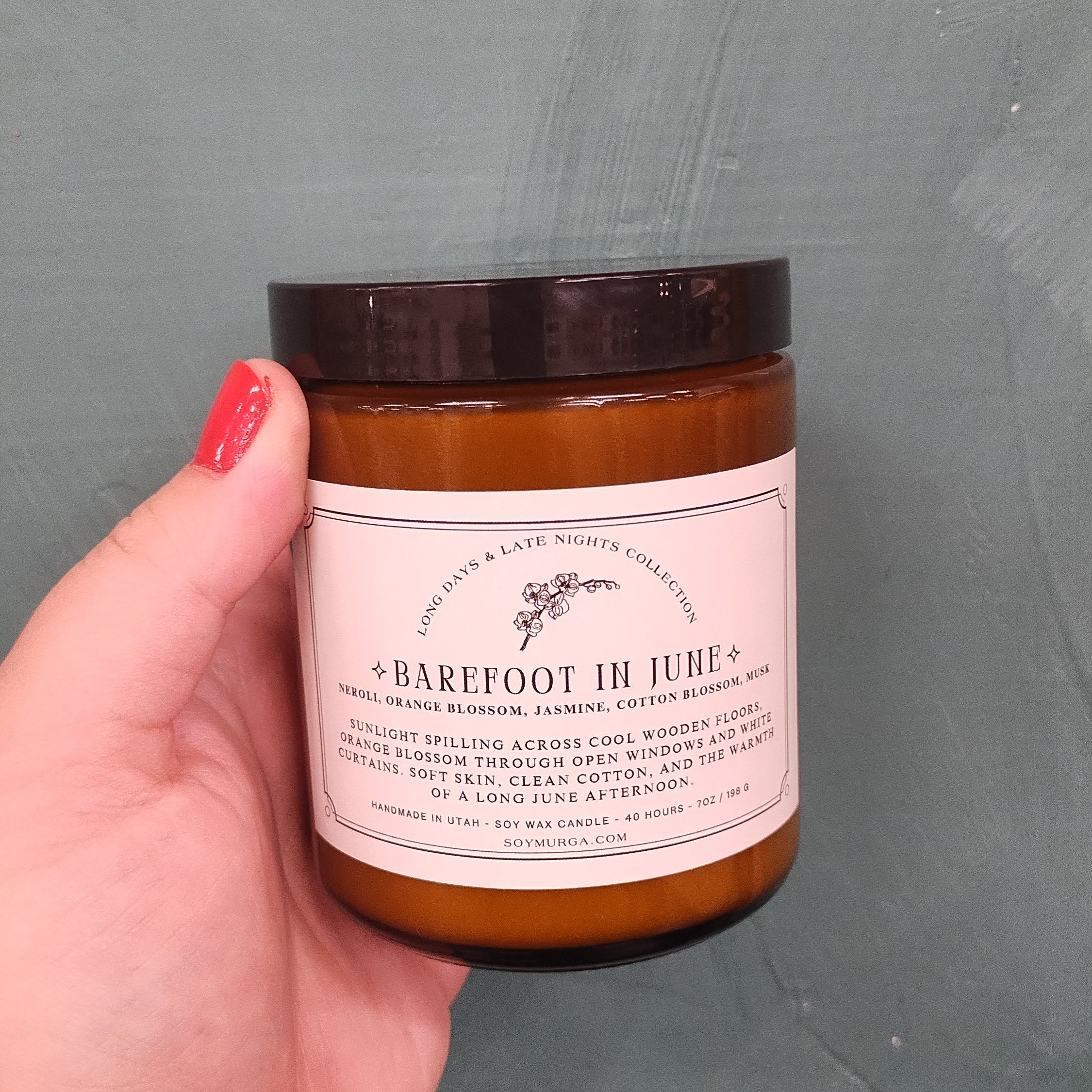 Amber jar with black lid and cream label. Held in woman's hand against a teal backdrop.