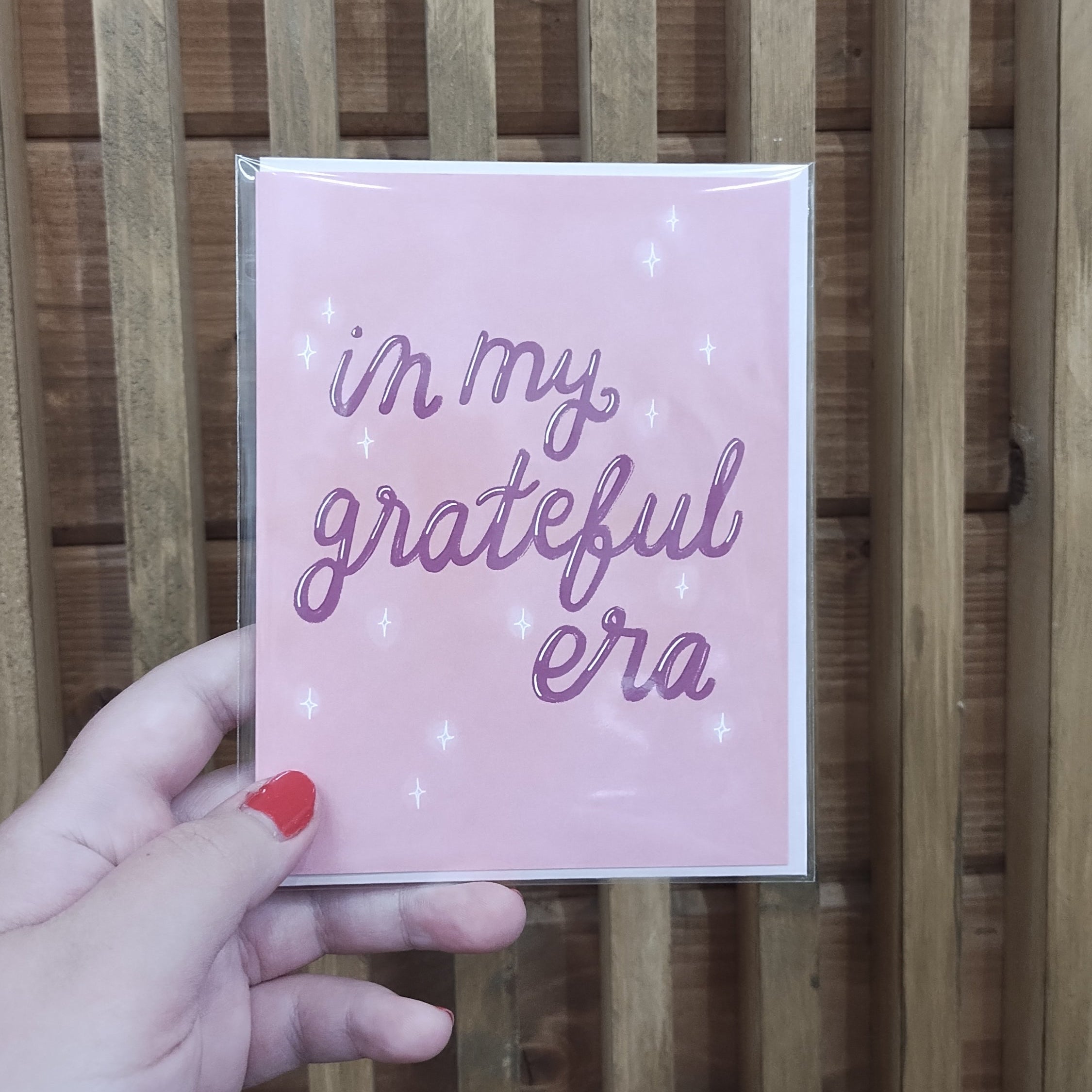 Pink card with purple cursive lettering saying in my grateful era. Sparkles drawn on design.