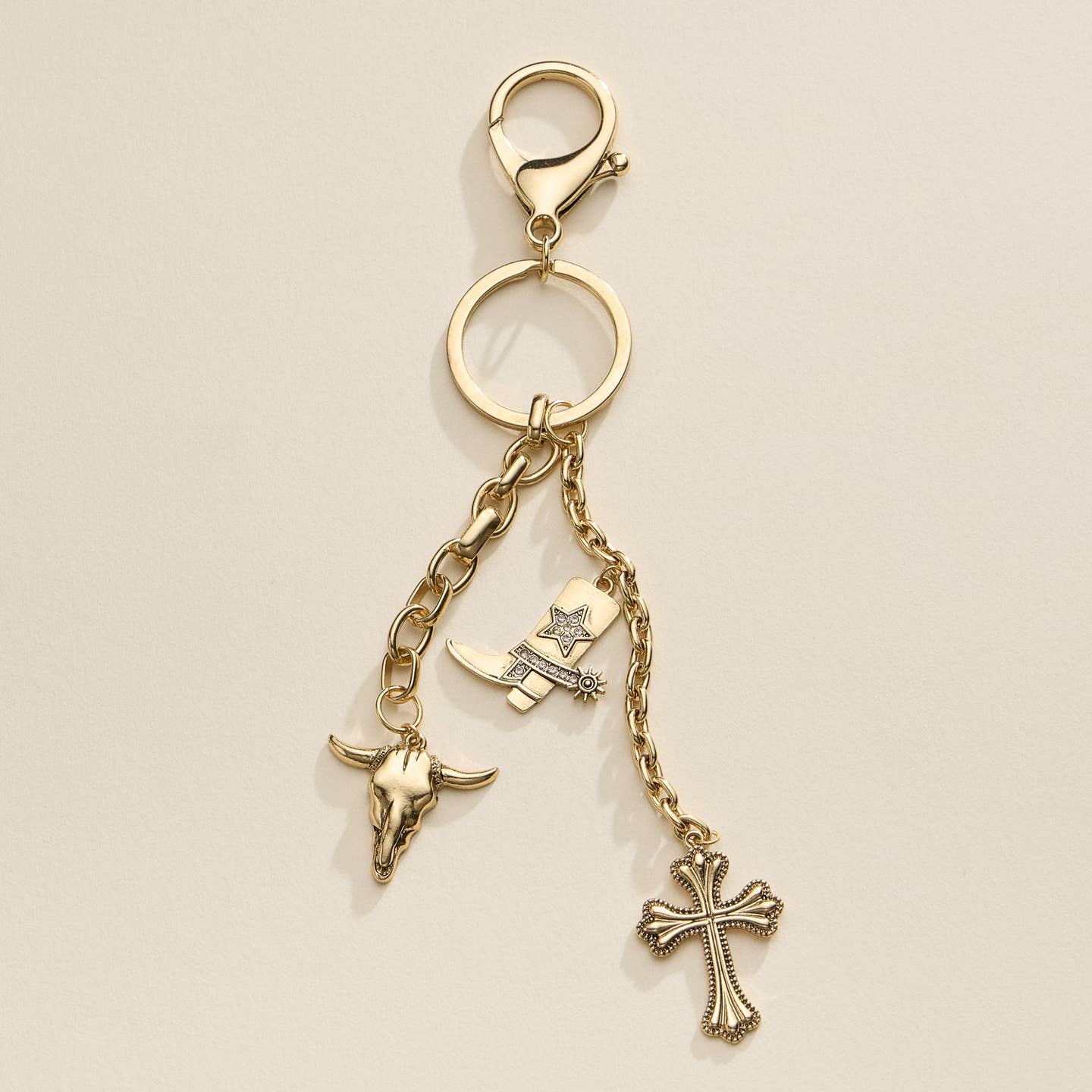 Embrace the western spirit with this stylish charm keychain featuring a cowboy boot, bull skull, and ornate cross. A perfect accessory for bags or keys. Shop now for a unique touch.