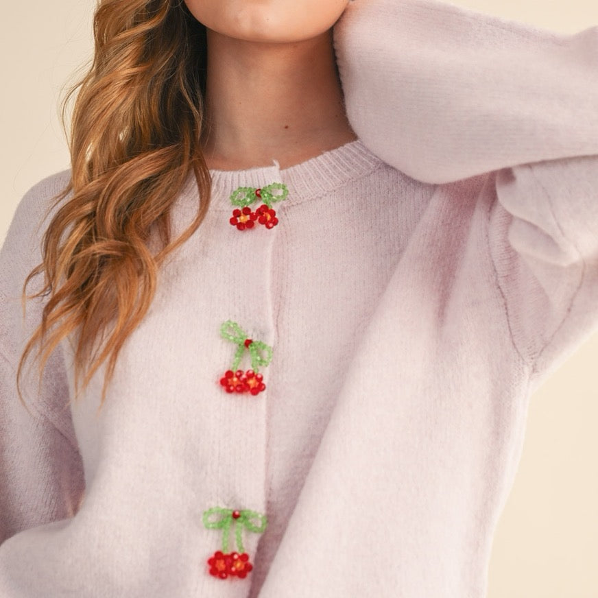 Elevate your everyday style with this charming cardigan featuring soft pink tones and delicate beaded bow and floral button details. Each button is a miniature work of art, adding a whimsical touch to your wardrobe. Perfect for layering over dresses or pairing with your favorite jeans, this piece brings a feminine, thoughtful elegance to any outfit. The supportive structure and quality construction ensure you'll reach for it again and again, making it a versatile staple.