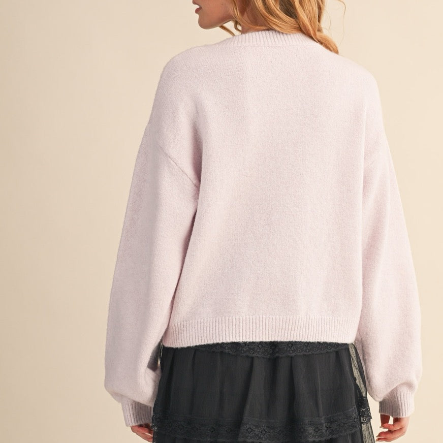 Elevate your everyday style with this charming cardigan featuring soft pink tones and delicate beaded bow and floral button details. Each button is a miniature work of art, adding a whimsical touch to your wardrobe. Perfect for layering over dresses or pairing with your favorite jeans, this piece brings a feminine, thoughtful elegance to any outfit. The supportive structure and quality construction ensure you'll reach for it again and again, making it a versatile staple.