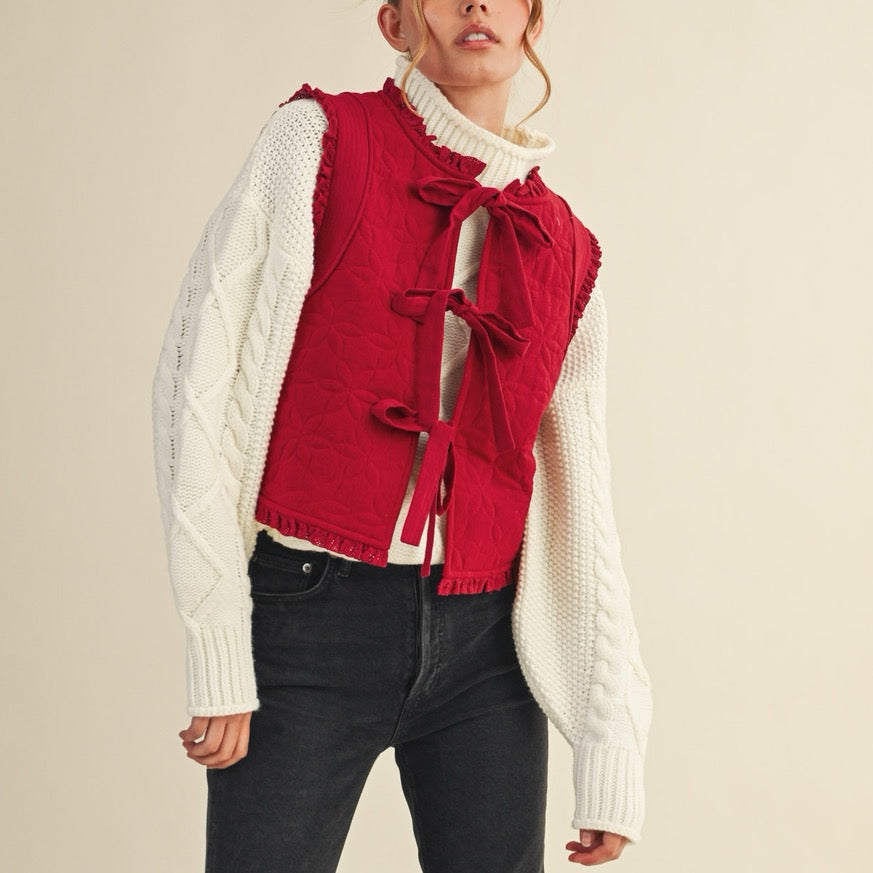 Elevate your layering game with this charming red floral quilted vest. Crafted from soft quilted fabric adorned with delicate floral patterns, it features a front-tie closure that lets you customize the fit to your comfort. The pretty lace trim adds a touch of feminine elegance to any outfit. Perfect for layering over your favorite tees or dresses, this versatile piece brings warmth and style to your everyday wardrobe.