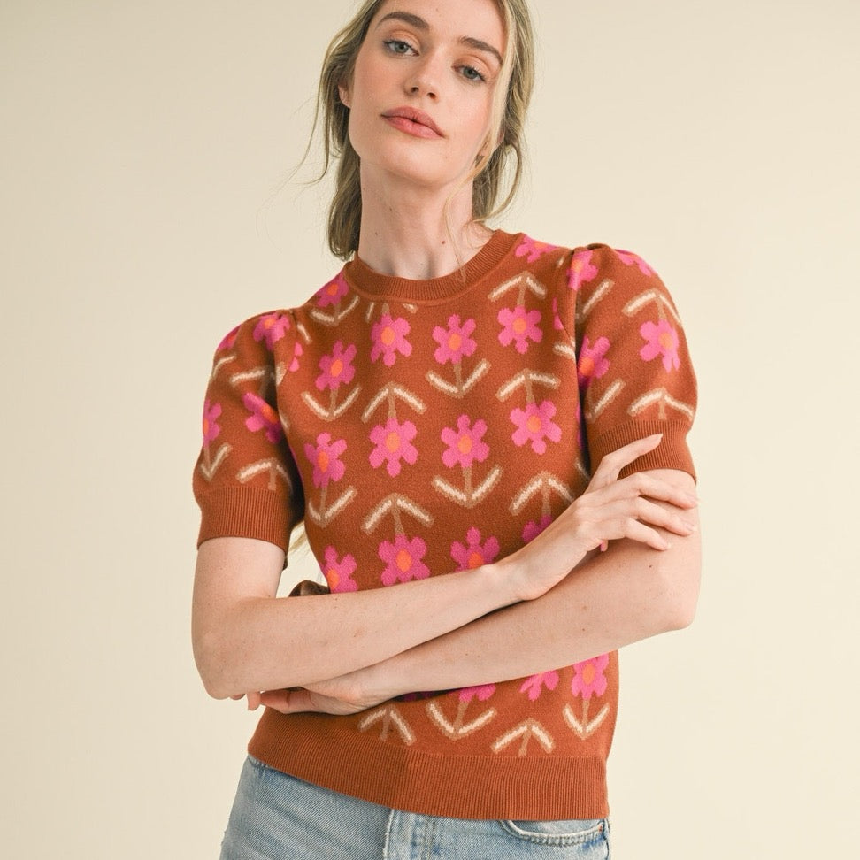 Embrace effortless style with this charming short sleeve knit sweater in warm mocha tones. Delicate pink flowers dance across the fabric, adding a touch of natural beauty to your everyday wardrobe. The soft, breathable knit construction keeps you comfortable whether you're layering for cooler days or wearing it solo when temperatures rise. Perfect for transitional seasons, this versatile piece pairs beautifully with jeans, skirts, or trousers for a look that feels both polished and approachable.