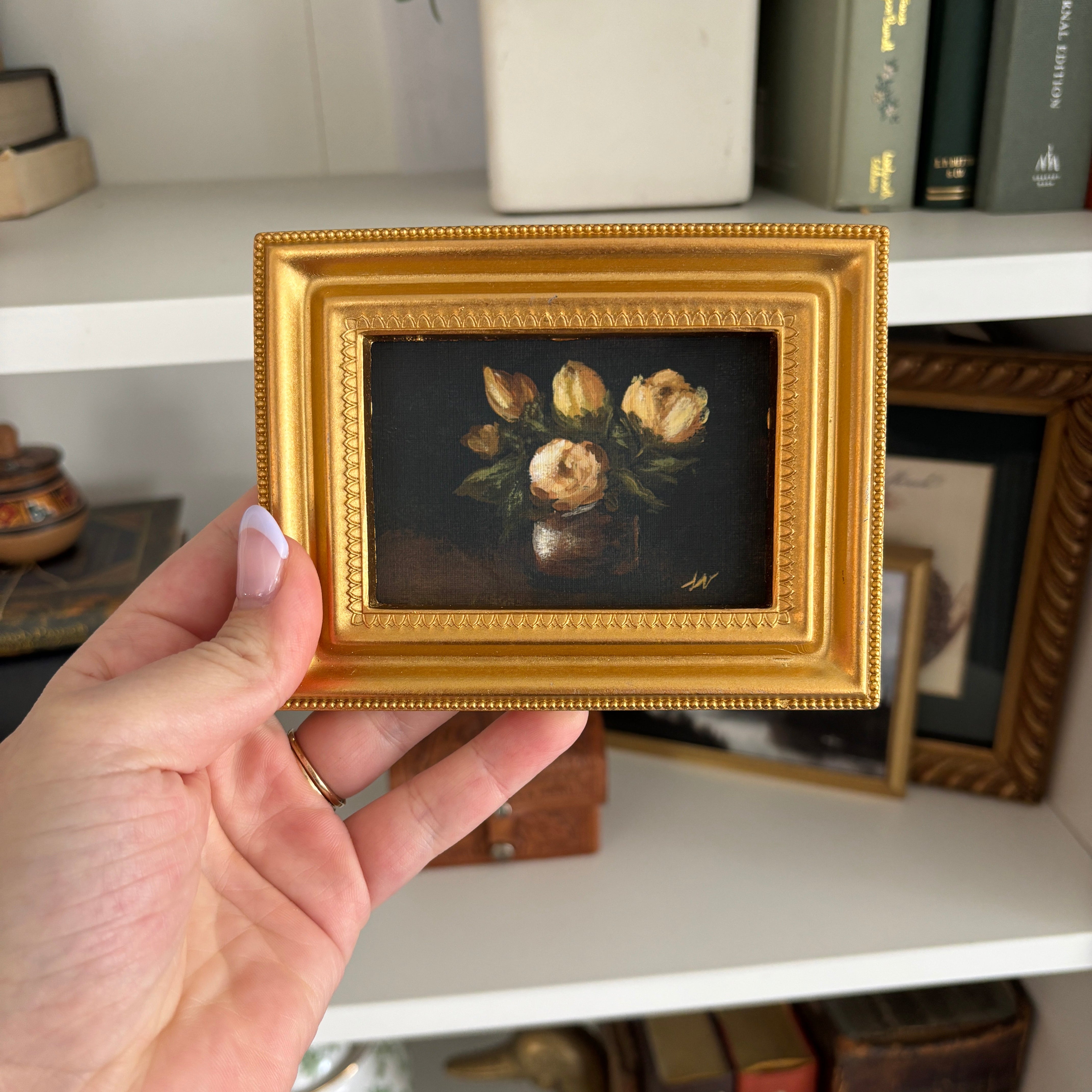 Gold frame on the art print, held in woman's hand with a bookcase in the background