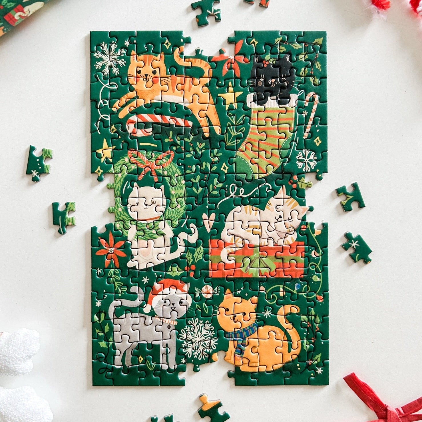 Partially completed puzzle against a white surface. Puzzle depicts 6 cats playing with Christmas decor and gifts.