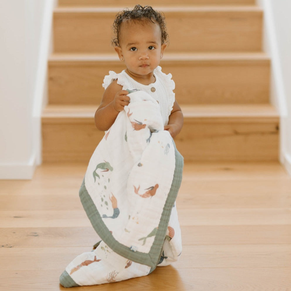Say hello to this cute baby quilt, certain to be a favorite in your little one's blanket collection. Made from three layers of 100% cotton muslin, it's just as durable as it is soft, cozy and breathable. Perfectly sized for snuggles, tummy time or on-the-go in your favorite stroller or jogger. Printed on both sides with our signature artwork for a beautiful touch to any nursery, and as a perfect shower gift. Cotton Muslin Baby Quilt - Mermaids.      Materials  100% cotton muslin.