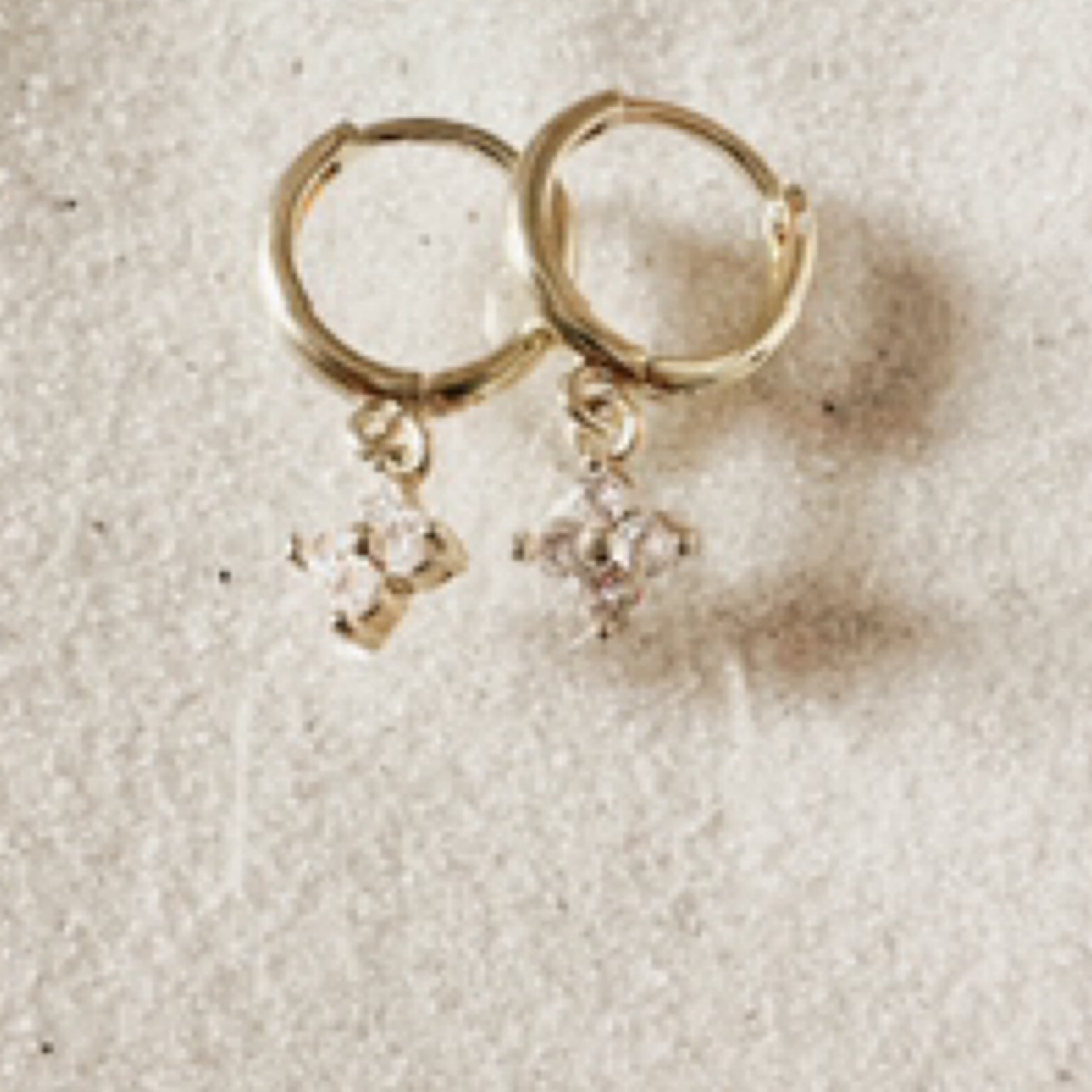 Gold hoops with a 4 petal crystal flower charm. Pictured against white sand.