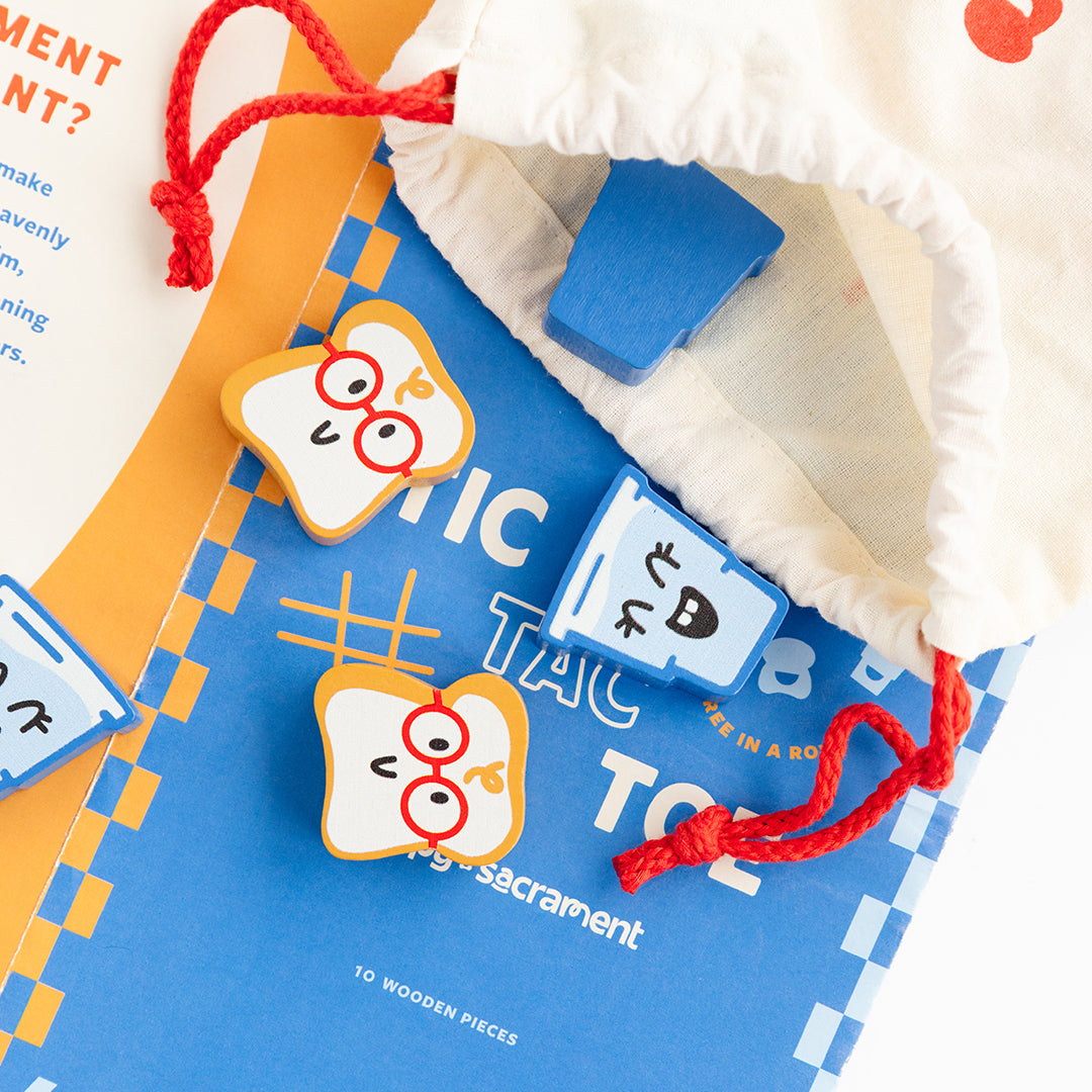 A blue and orange Tic Tac Toe game is shown with wooden game pieces featuring playful illustrated designs. The pieces are partially arranged on the game board beside an open cream-colored drawstring pouch with red cords.