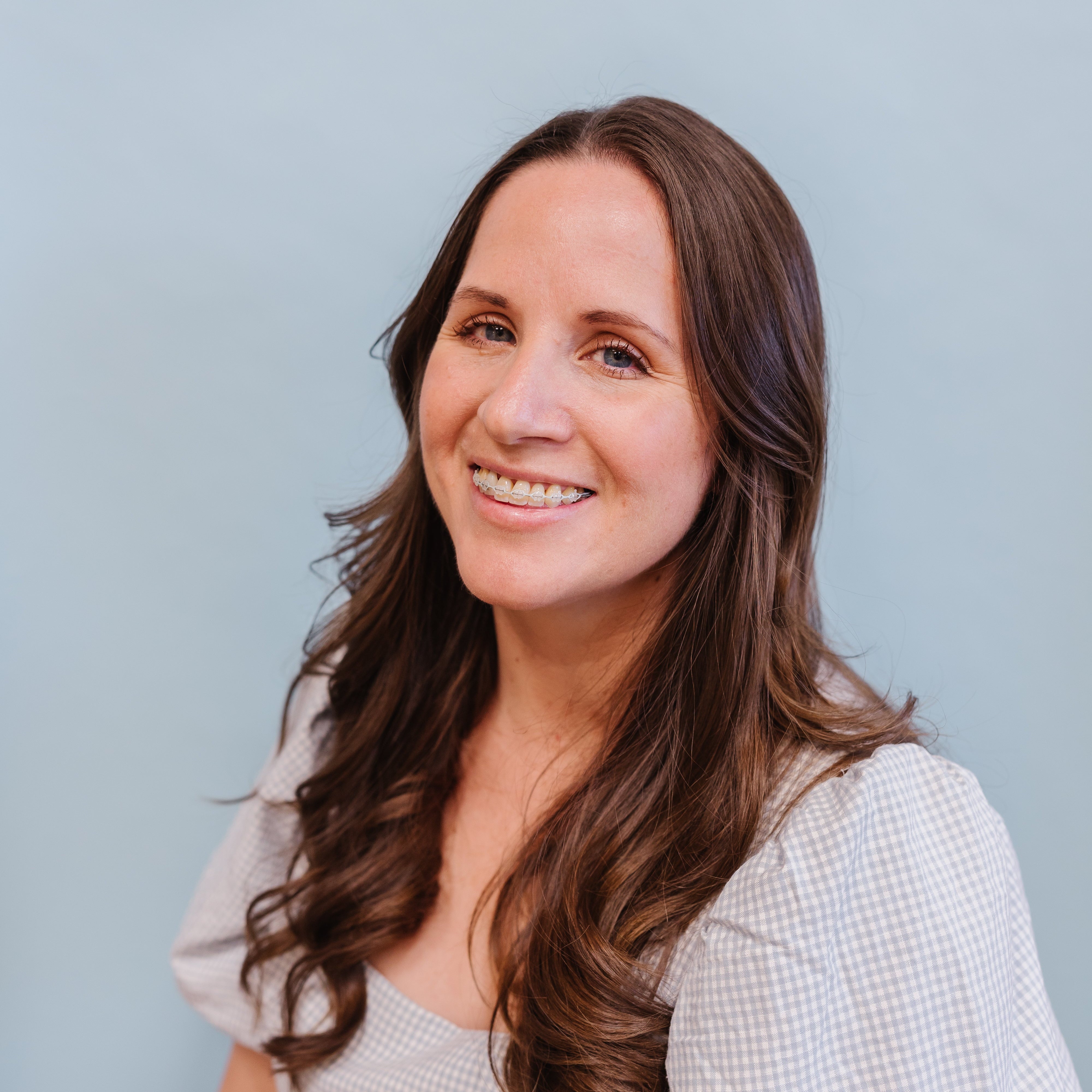 Woman with long brown hair smiling against a light blue background