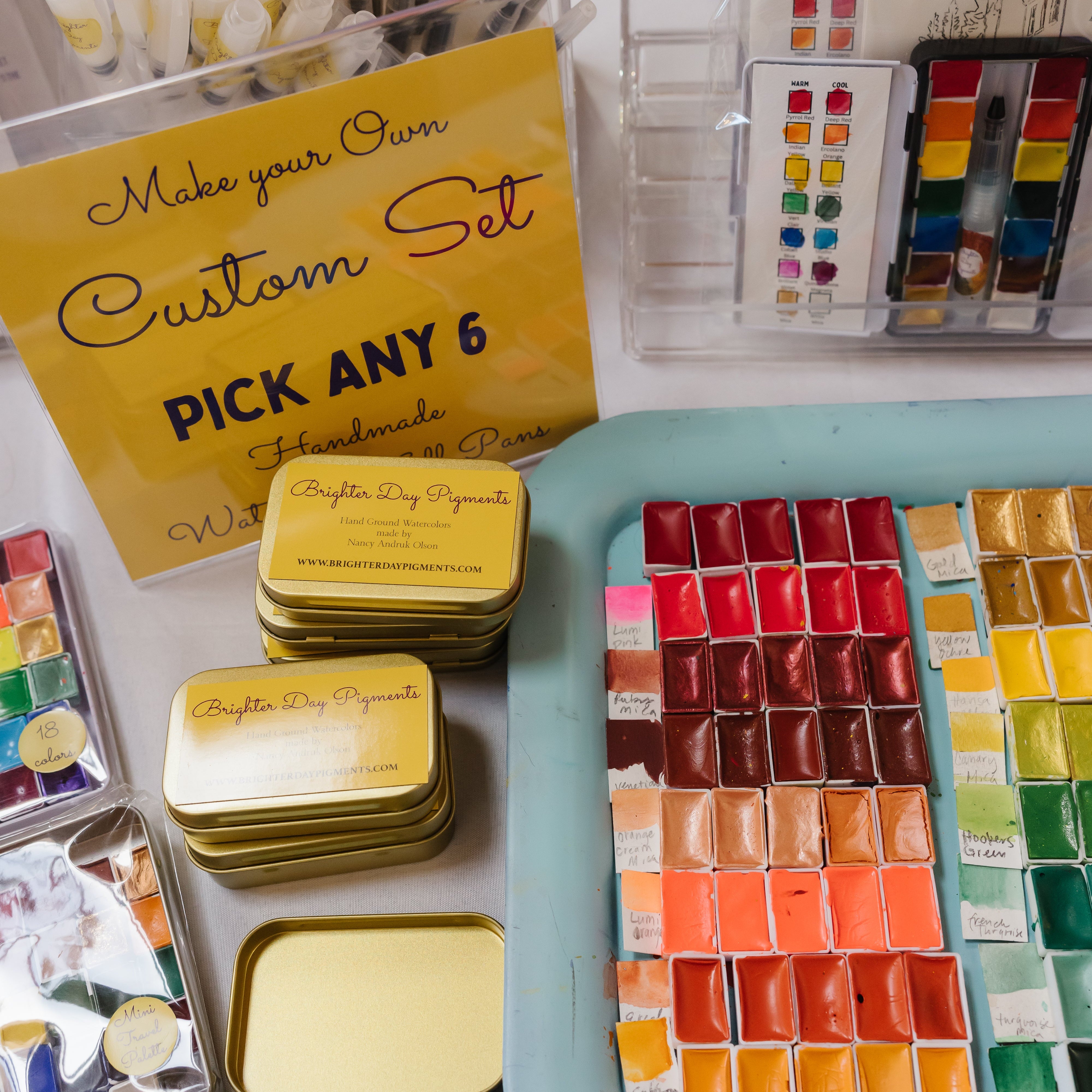 Collection of watercolor paint sets and custom set options on a white surface.