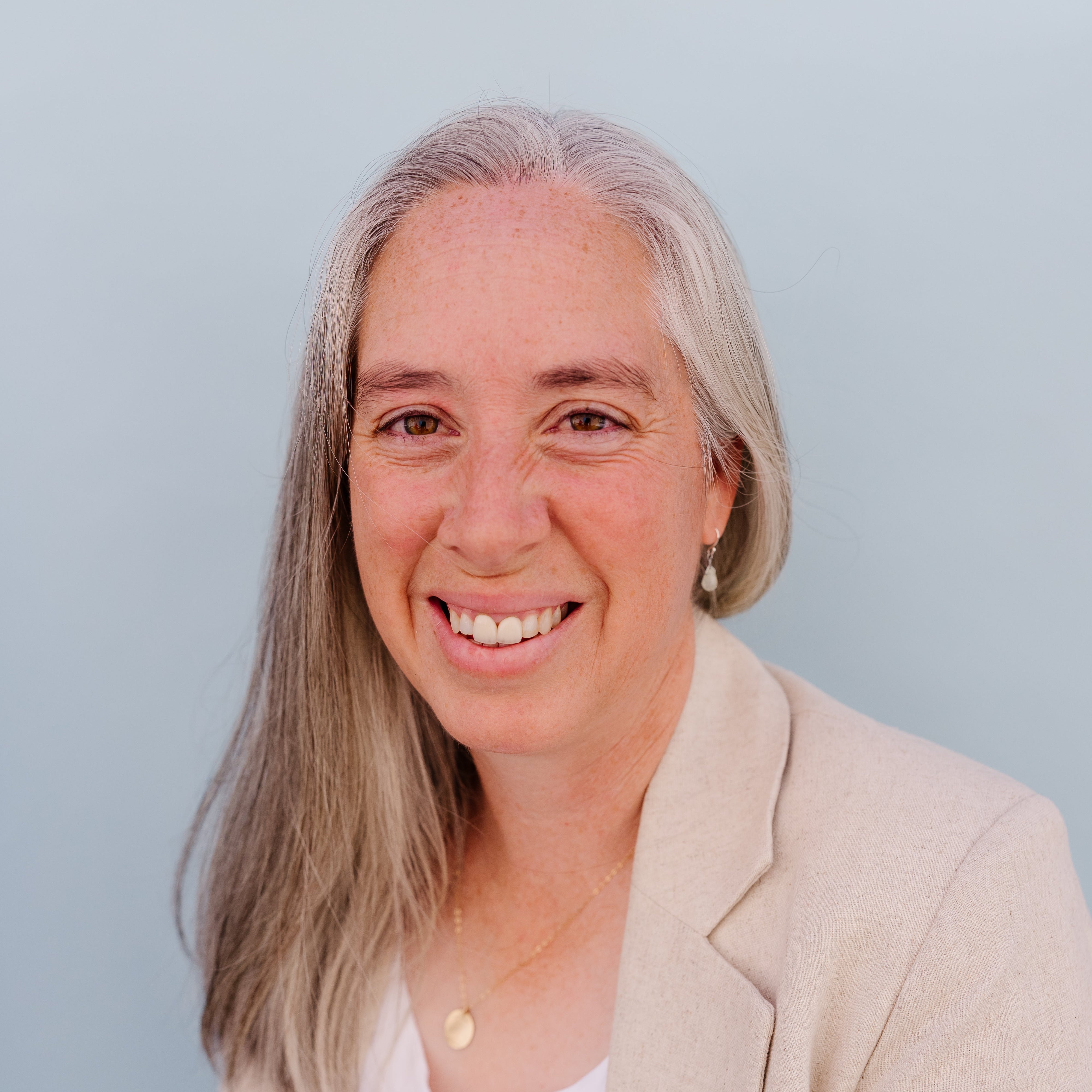 Woman with gray hair wearing a beige blazer against a light blue background