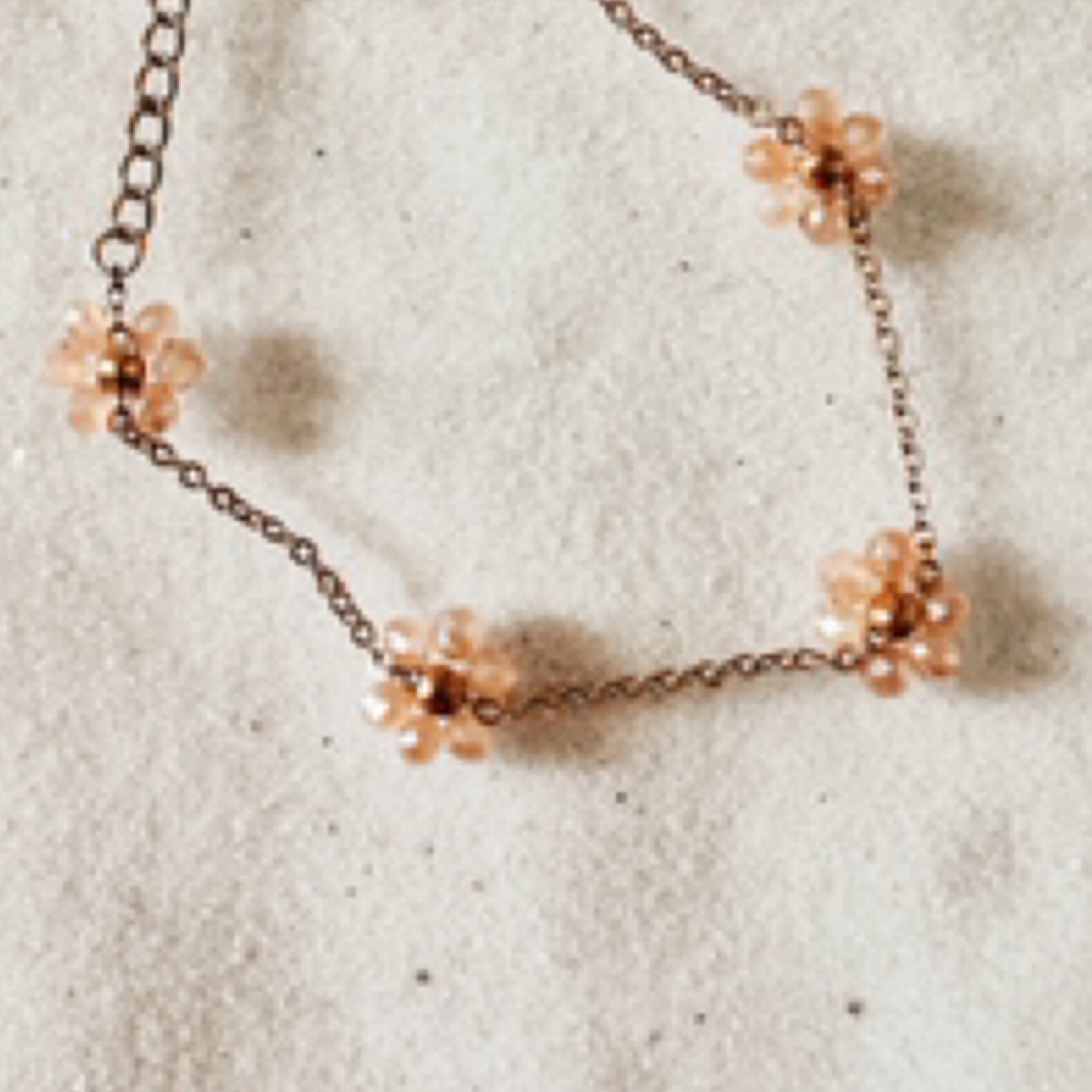 Delicate gold chain with champagne colored sparkly stones clustered together like daisy petals around a gold bead as the center of the daisy. (total of 4 daisies per bracelet). Pictured against white sand.
