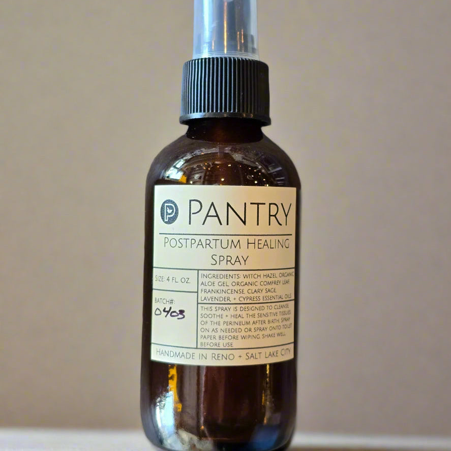 Dark amber spray bottle with cream label and black font against an off white wall.