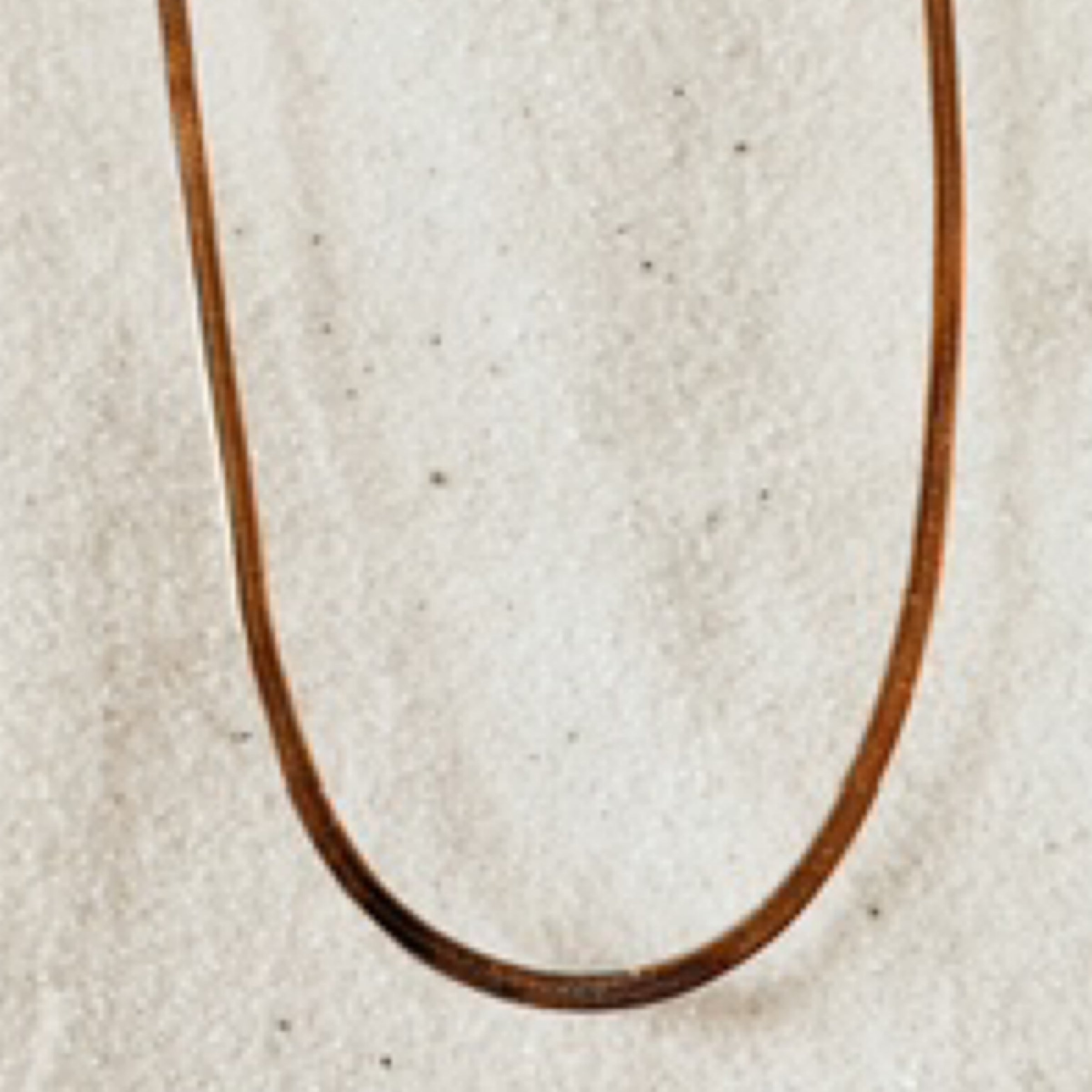Delicate skinny gold snake chain pictured against white sand.