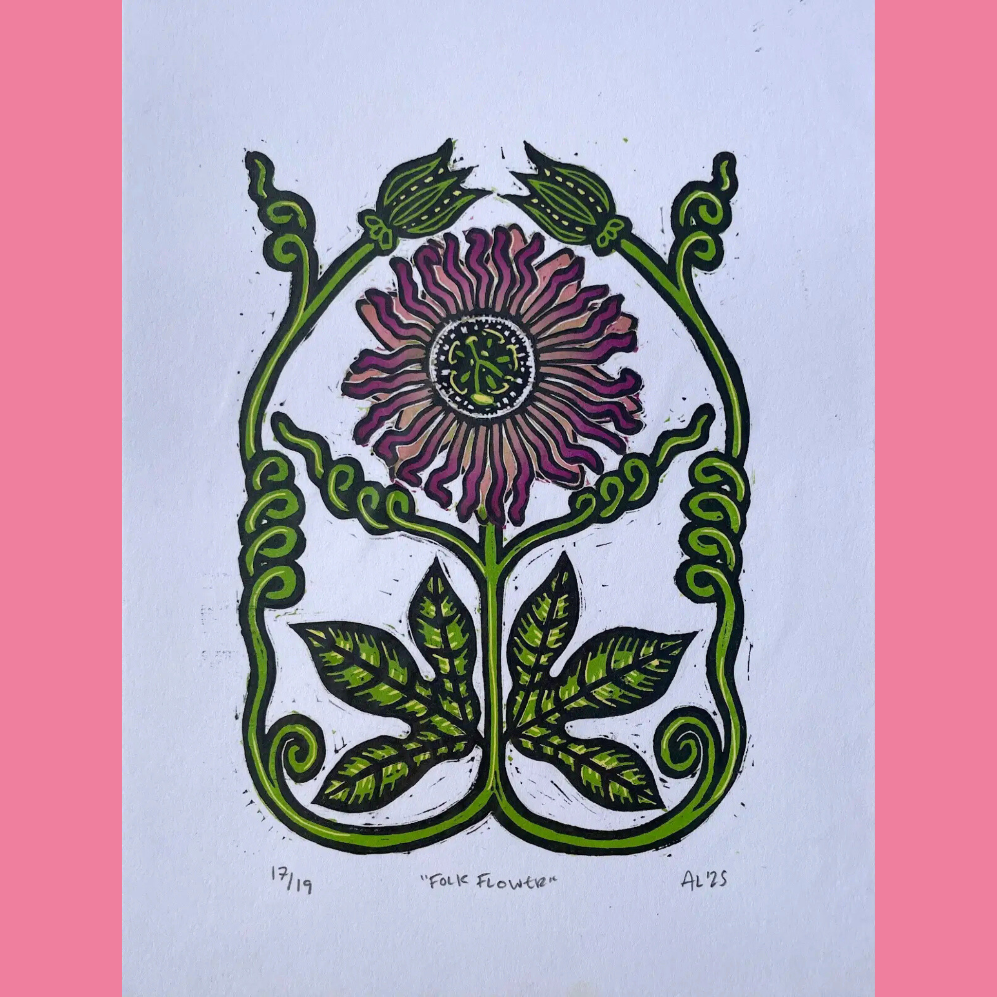A colorful linocut print shows a stylized folk-inspired flower in shades of purple, pink, and tan with a detailed circular center and wavy petals, framed by symmetrical curling green vines and broad palmate leaves at the base forming an elegant arched shape. The artwork is printed on white paper with the edition number "17/19," the title ""FOLK FLOWER"", and the signature "AL '25" handwritten below, surrounded by a bright pink border.