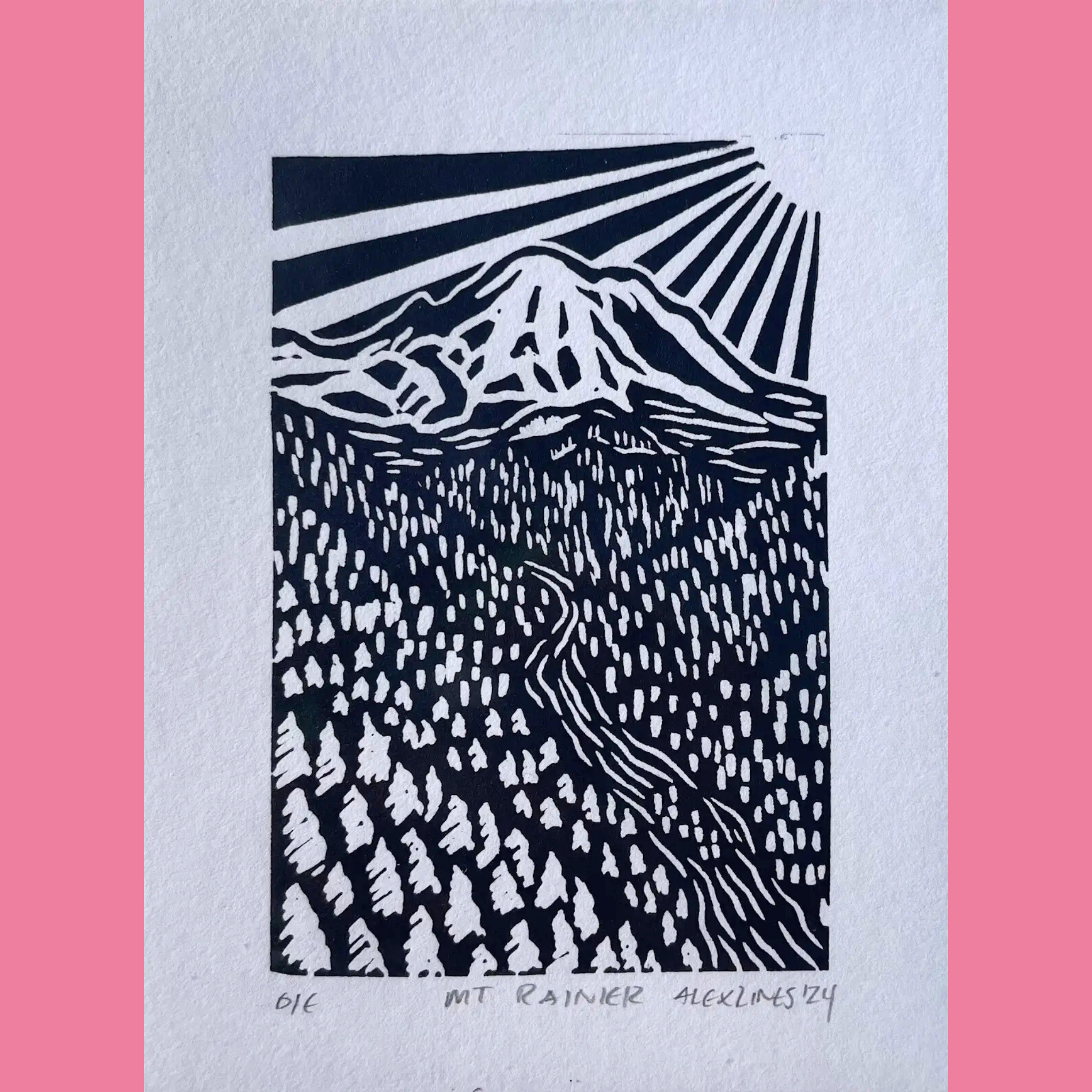 A black-and-white linocut print depicts Mount Rainier with dramatic radiating sunbeams bursting from behind its snow-capped peak, set against a dark sky at the top and a dense forest of detailed evergreen trees filling the lower half of the composition. The artwork is printed on white paper with the title "MT RAINIER," the number "016," and the signature "ALEX LINES '24" written below, surrounded by a bright pink border.
