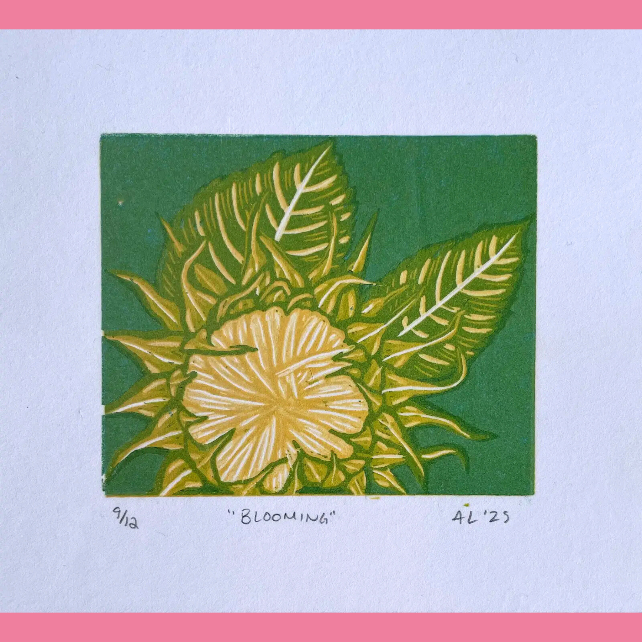 A vibrant linocut print in yellow and green features a large, radiant hibiscus-like flower in full bloom with layered petals and delicate veining, surrounded by broad, pointed tropical leaves with prominent white veins against a solid green background. The artwork is printed on white paper with the edition number "9/12," the title ""BLOOMING"", and the signature "AL '25" handwritten below, framed by a bright pink border.