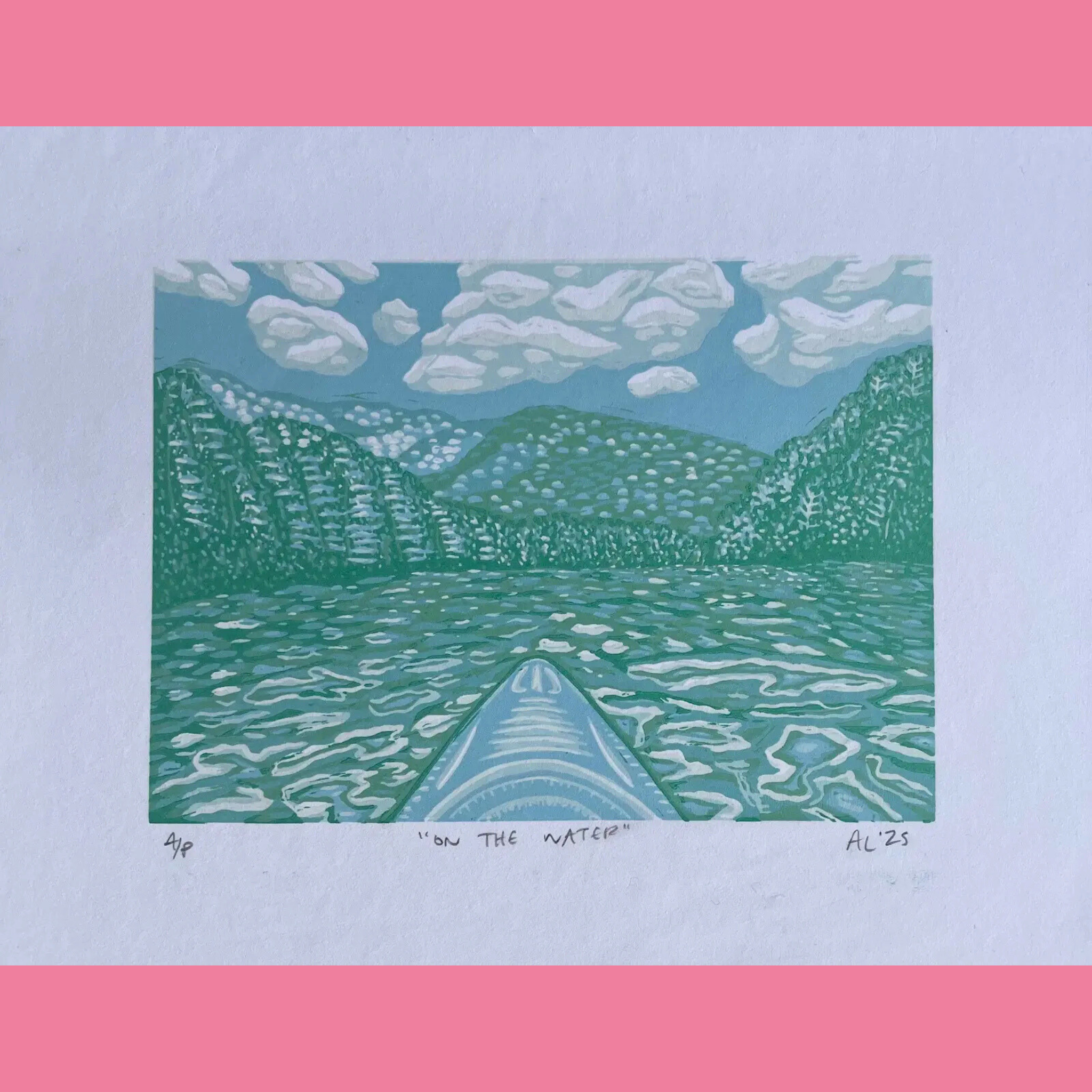 A colorful linocut print depicts a serene view from the bow of a canoe gliding across calm turquoise water, with gentle ripples spreading outward toward distant forested mountains under a light blue sky filled with soft white clouds. The composition is framed within a tall rectangular format on white paper, featuring the title ""ON THE WATER"" and the signature "AL '25" handwritten below, surrounded by a bright pink border.
