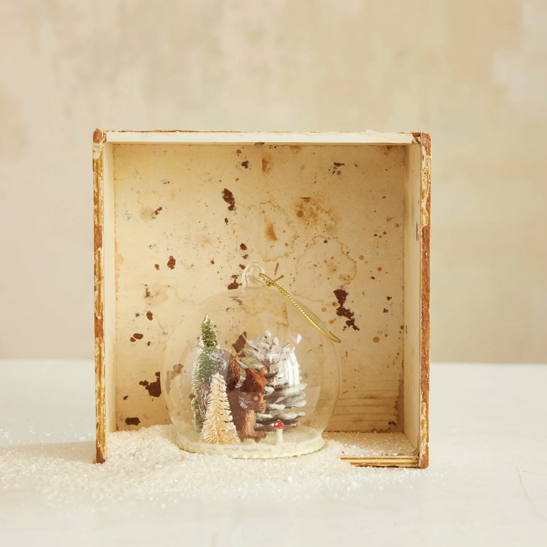 Decorative snow globe with trees inside a wooden box on a white surface.
