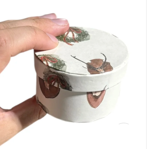 Hand holding a round container with deer design on a white background