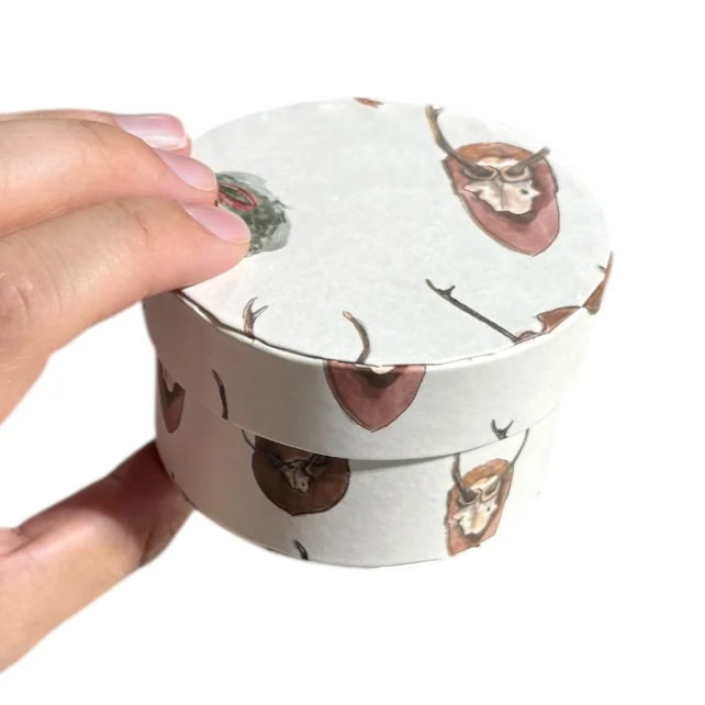 Hand holding a round container with deer design on a white background