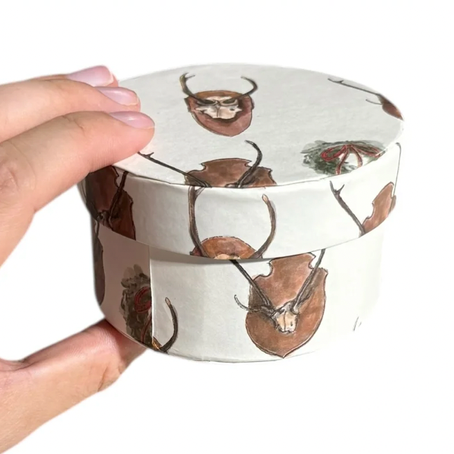 Hand holding a round container with deer design on a white background