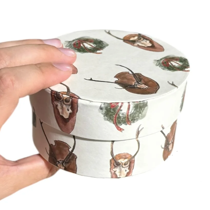 Hand holding a round container with deer design on a white background