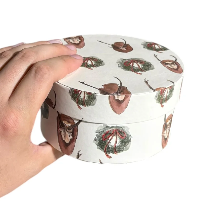 Hand holding a round container with deer design on a white background