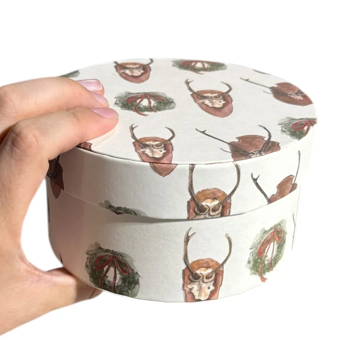 Hand holding a round container with deer design on a white background