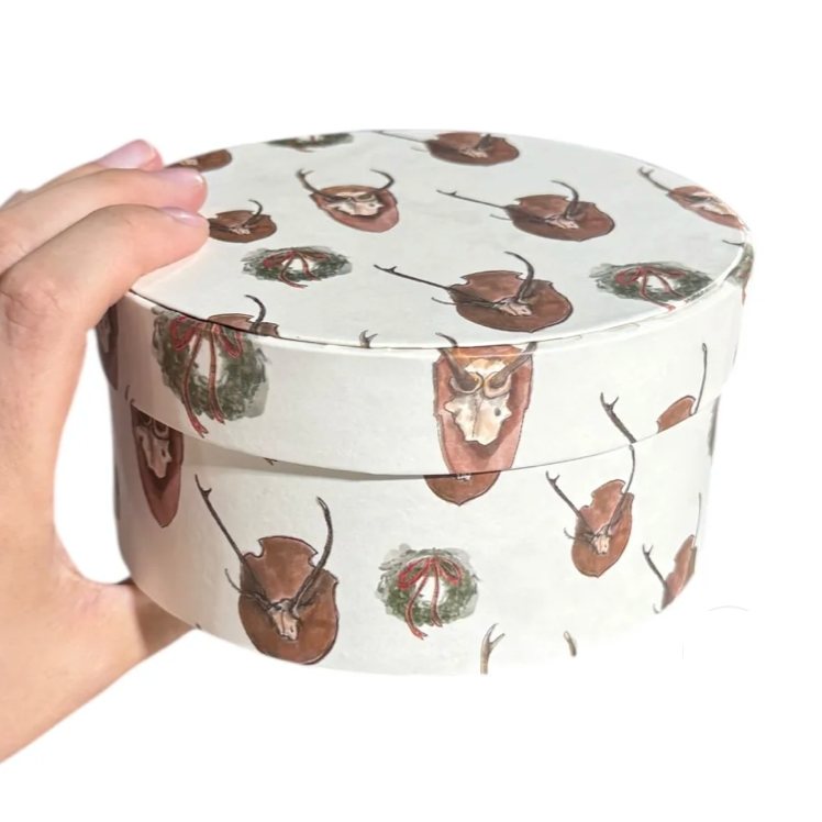 Hand holding a round container with deer design on a white background