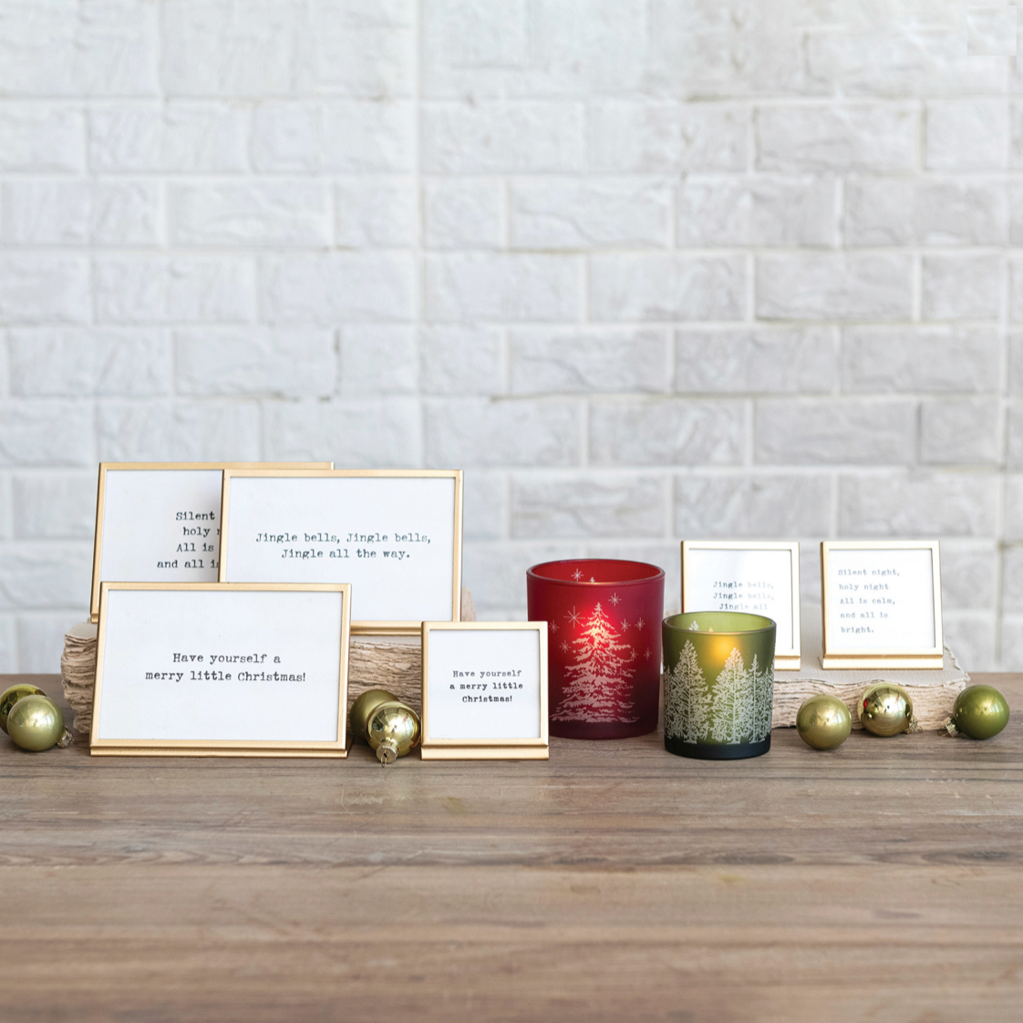 Decorative setup with candles, cards, and ornaments on a wooden surface against a brick wall.