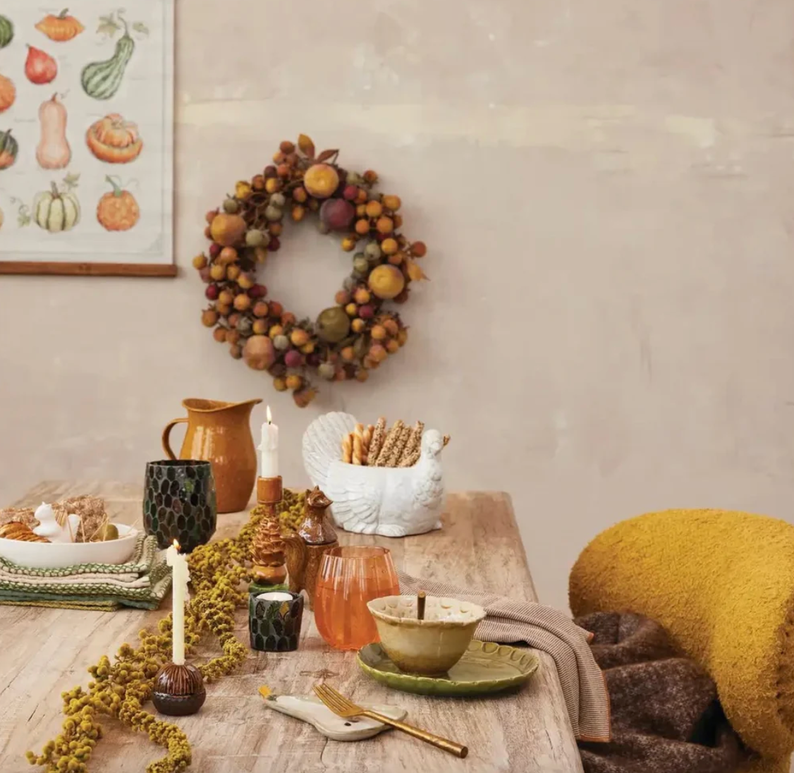 Autumn-themed decor with wreath, candles, and pumpkins on a table.