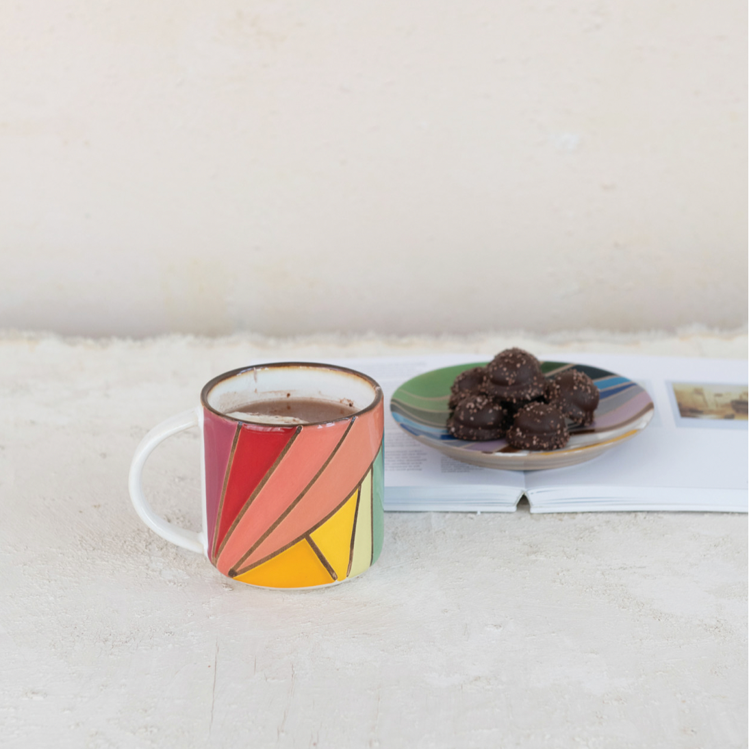 Colorful mug with coffee and a plate of cookies on a white surface