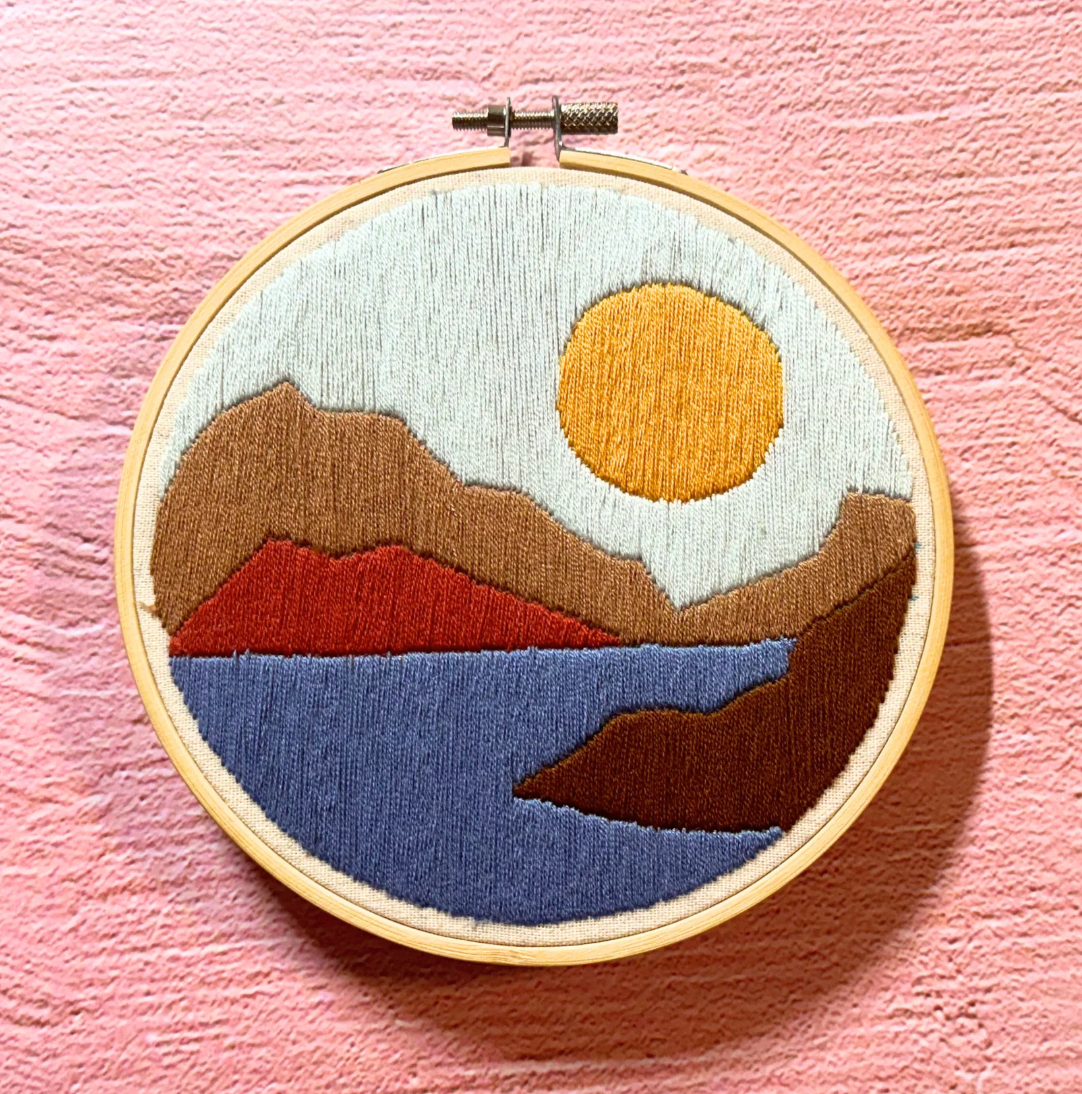 Embroidery hoop with a landscape design on a pink background