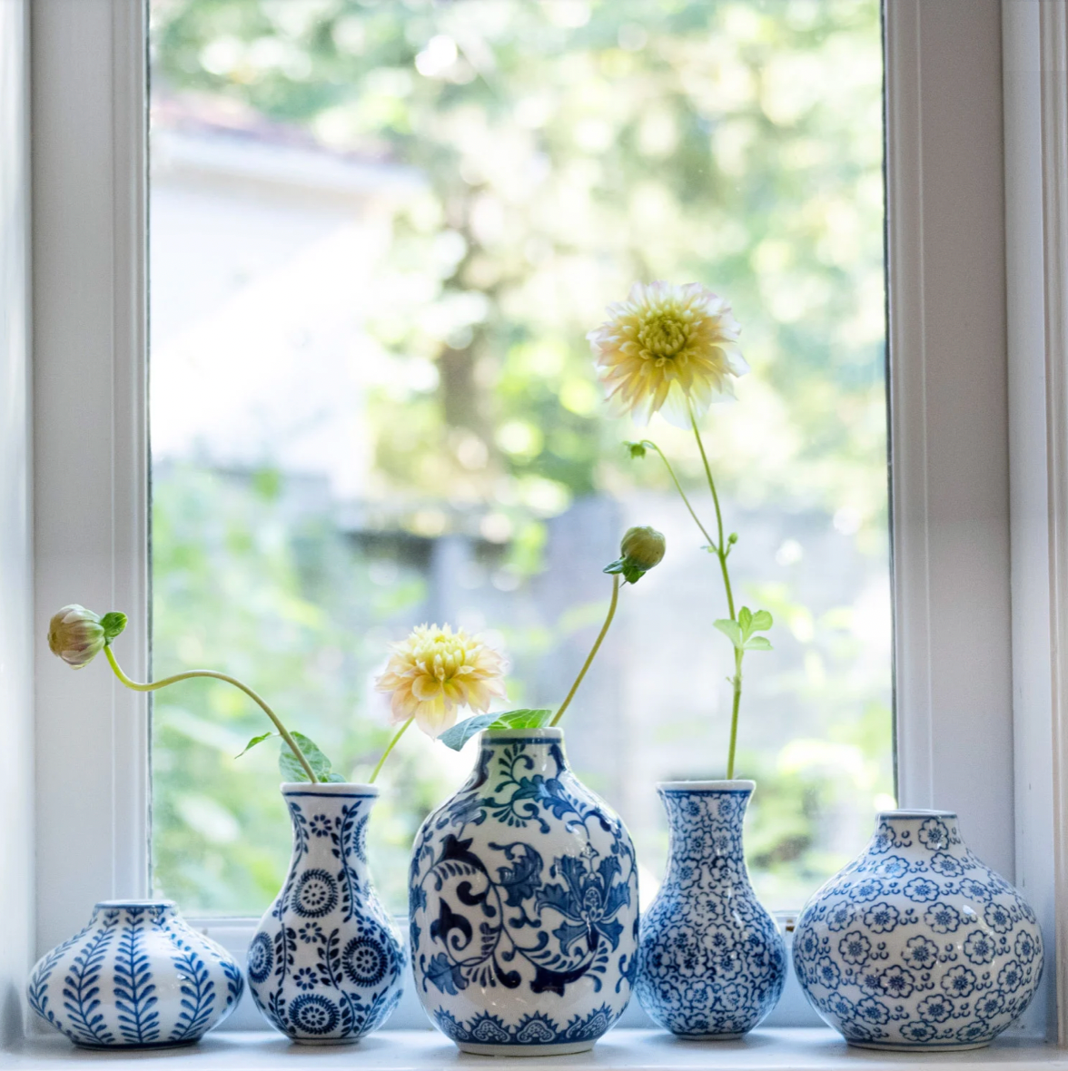 Set of blue and white patterned vases on a windowsill with flowers.