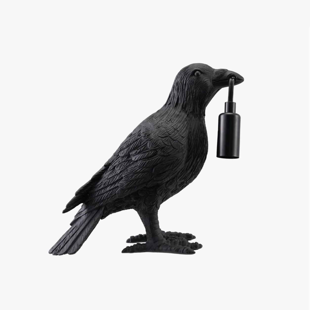 A black raven figurine holding a small black cylindrical light in its beak, photographed against a plain light gray background.