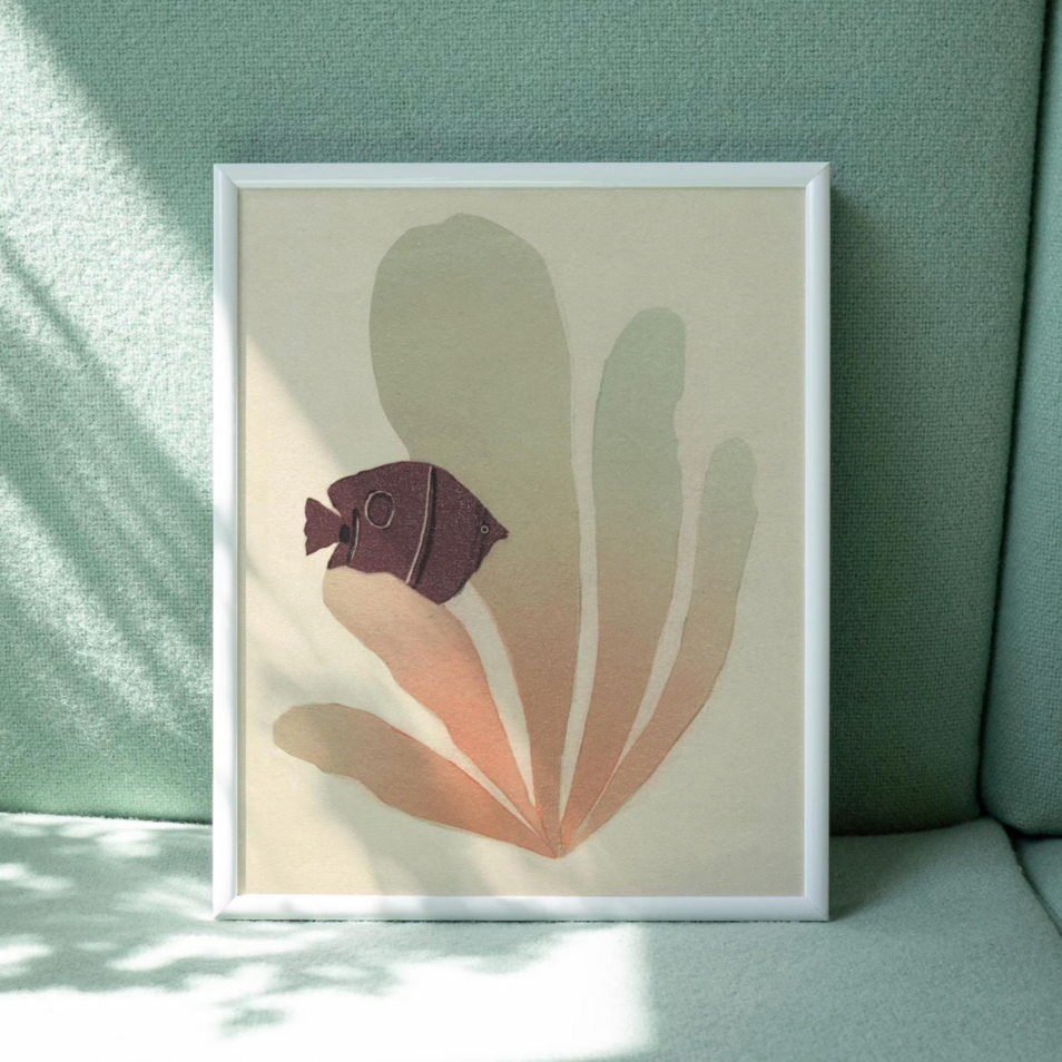 A framed art print featuring a stylized fish and leaf design in muted beige, blush, and plum tones, leaning against a mint green textured wall with soft window shadows.