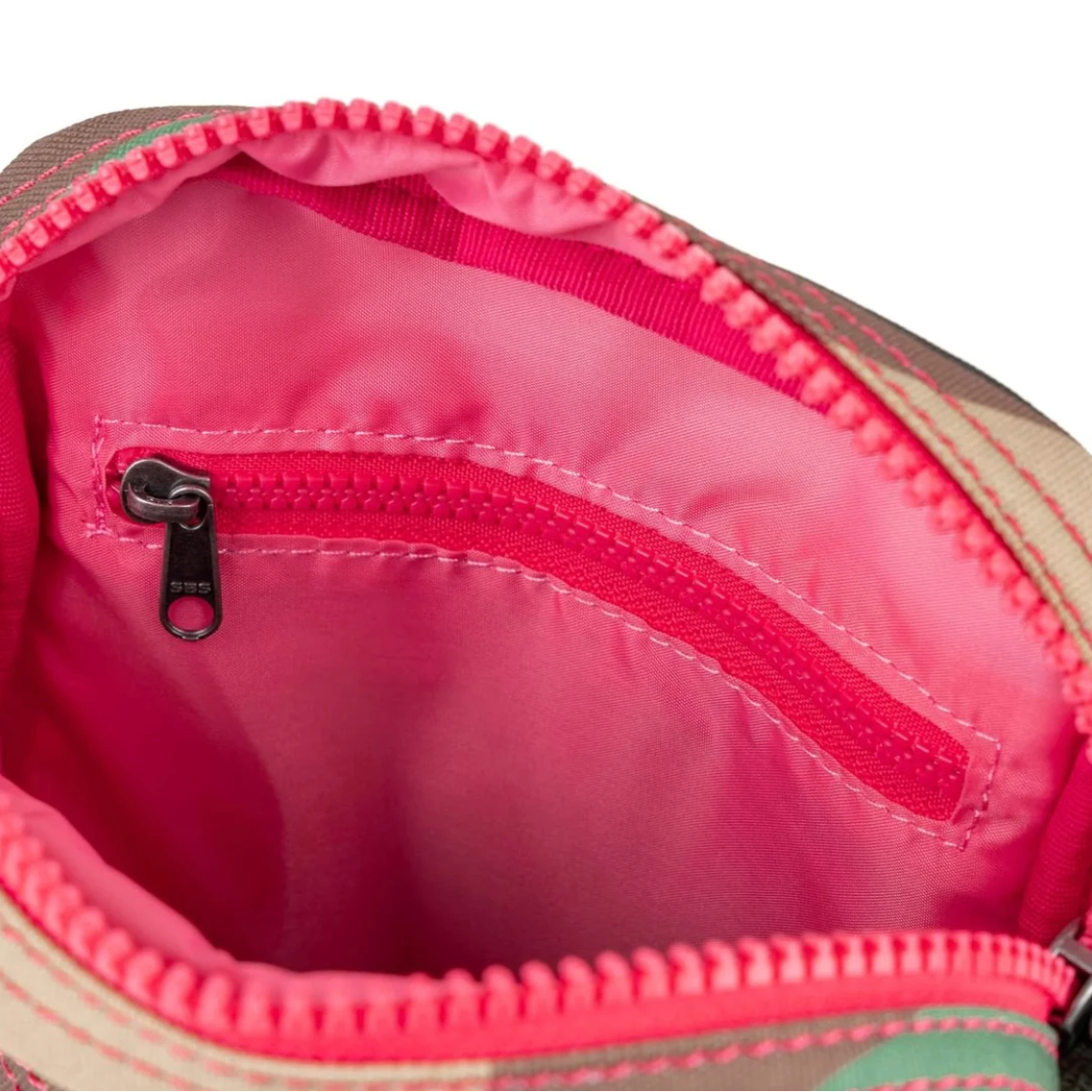 Close-up of the interior of a zippered pouch or bag, showing a bright pink nylon lining, a pink zipper track, and a beige fabric exterior edge with green stripe accents.