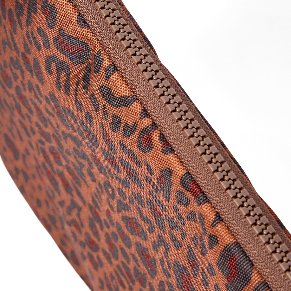 Close-up of a leopard print pouch or clutch in brown, black, and red tones, showing the woven fabric texture and a matching brown zipper on a white background.