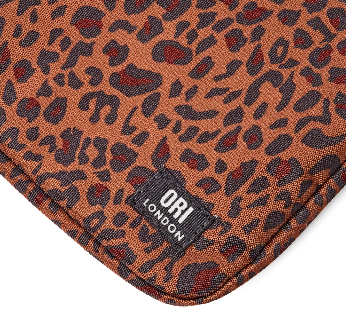 Close-up of a leopard print textile product corner with a black brand patch reading ORI LONDON, on a white background.