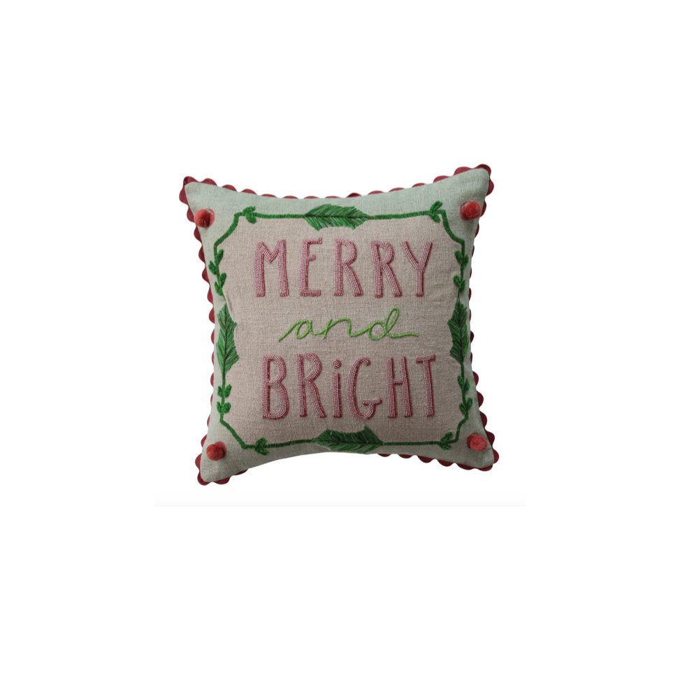 A square decorative throw pillow with a scalloped edge, featuring the embroidered text 'MERRY and BRIGHT' in pink and green on a light beige fabric background, accented with red pom-poms in the corners.