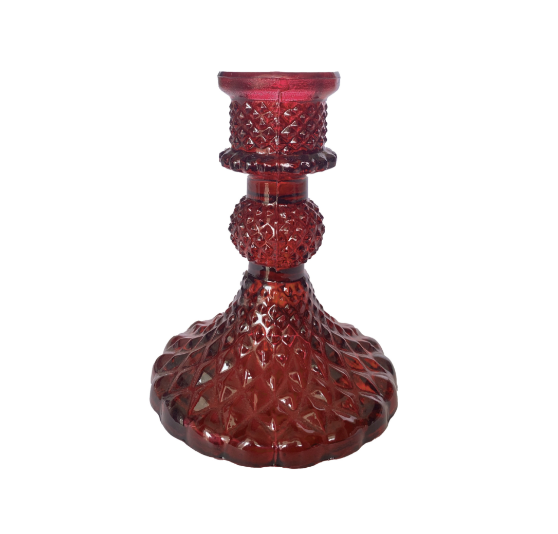 A vintage-style red glass candlestick holder with a textured, diamond-cut pattern on a solid white background.