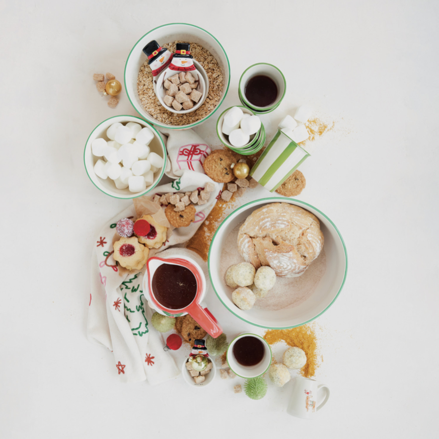 An overhead flat-lay of assorted holiday treats and coffee on a white background, including cookies, marshmallows, hot chocolate, pastries, and small gift boxes.